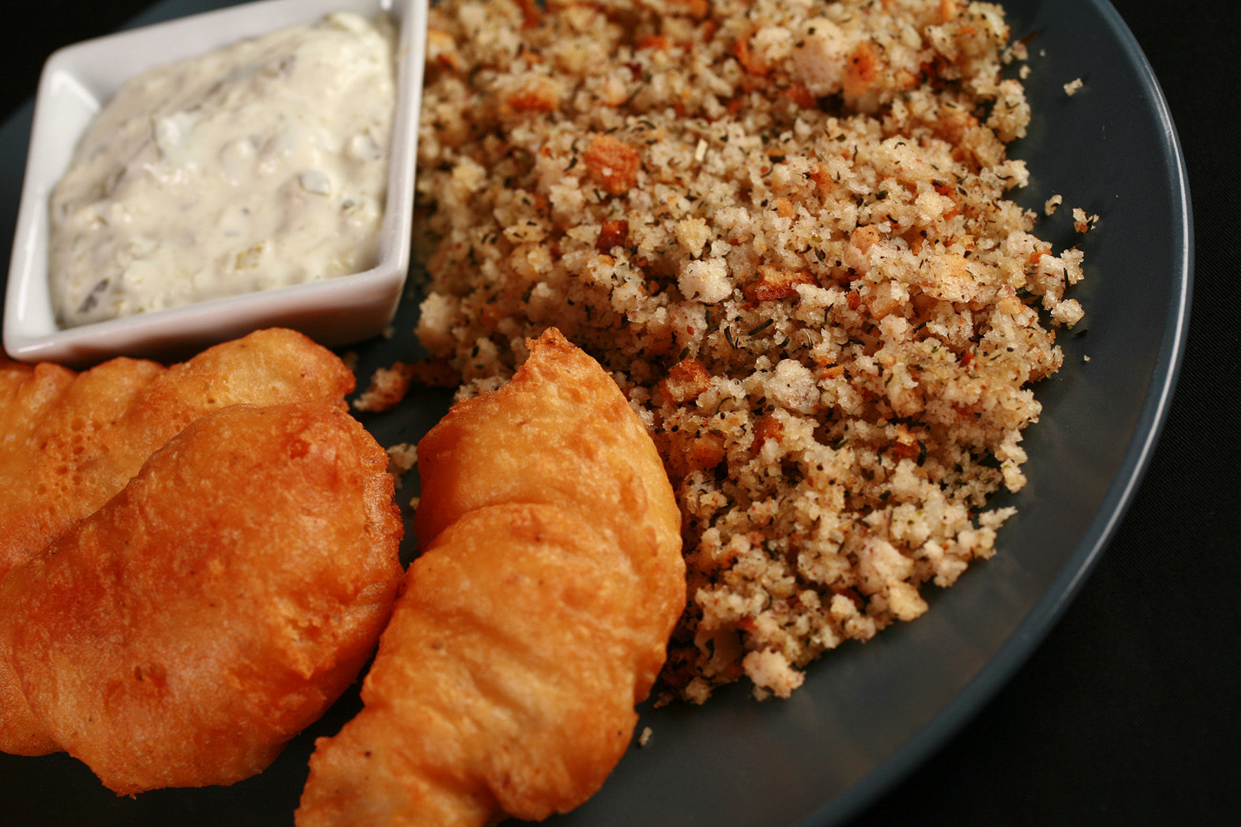 Gluten-Free Cod Cheeks and Dressing, on a round, blue plate. There is a small dish of tartar sauce on the plate, as well.