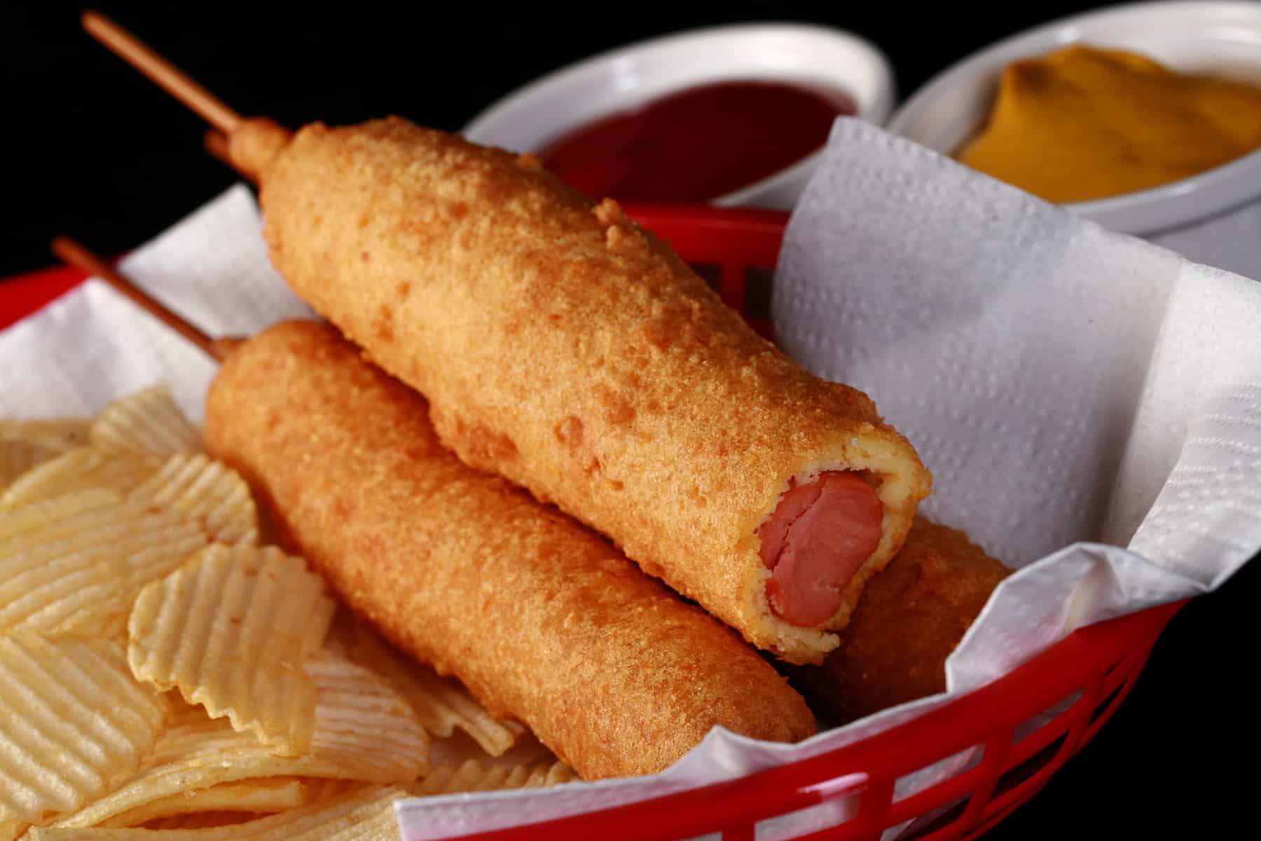 3 gluten-free corndogs in a basket with mustard and ketchup.
