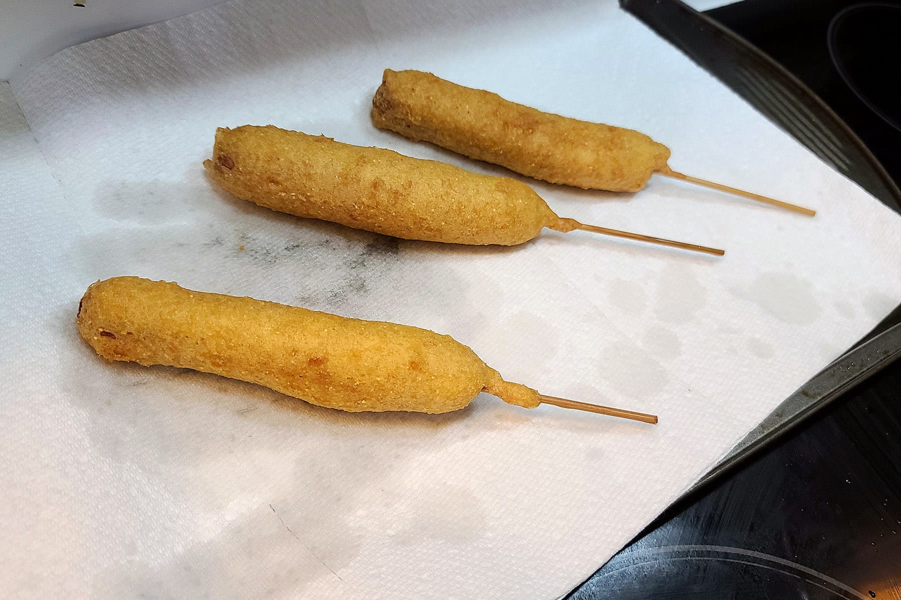 3 cooked gluten free corndogs on a paper towel lined baking pan.