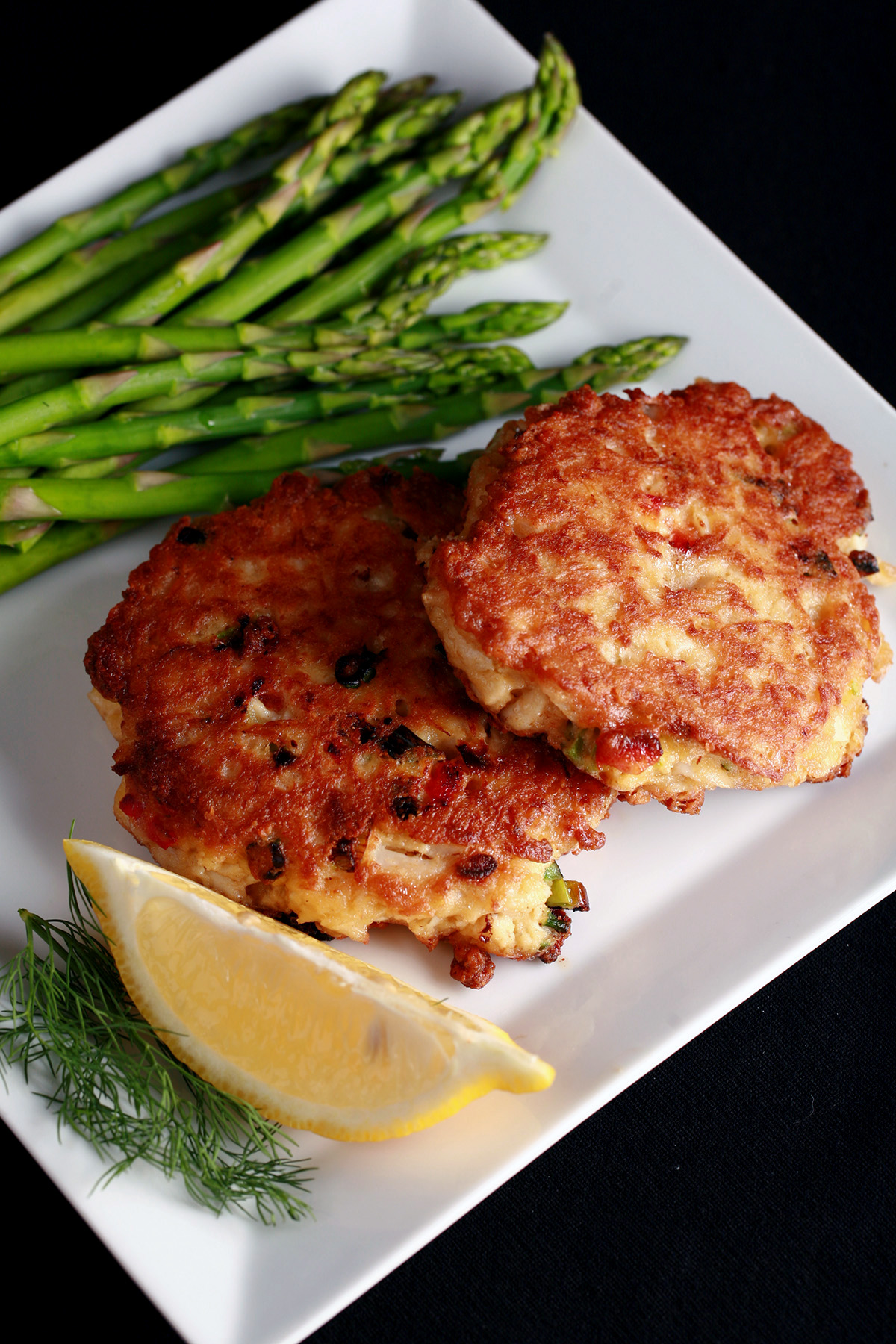 2 Gluten-free Crab Cakes on a plate with asparagus, a lemon slice, and some fresh dill.