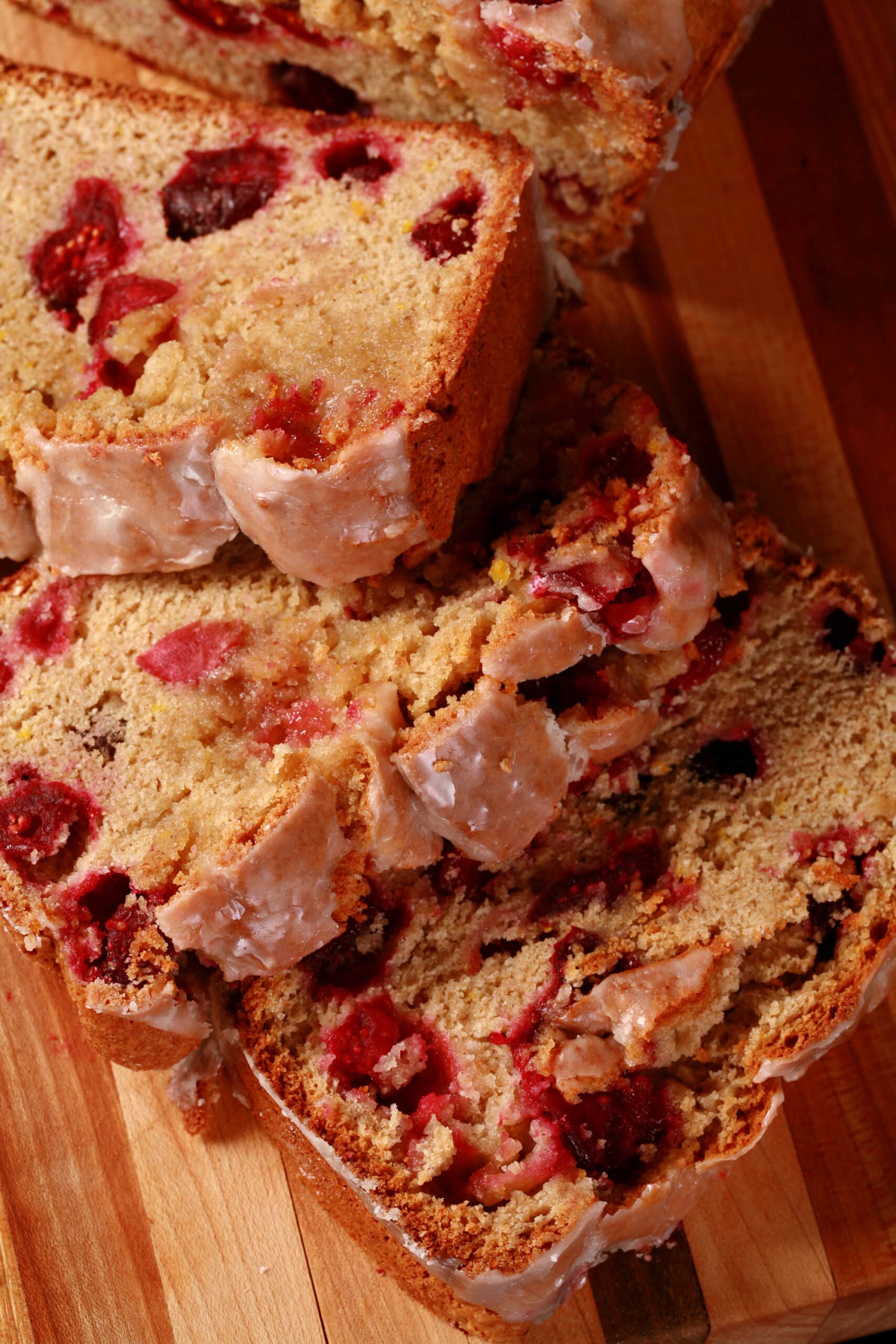 A loaf of glazed gluten-free cranberry orange bread, sliced on a cutting board.