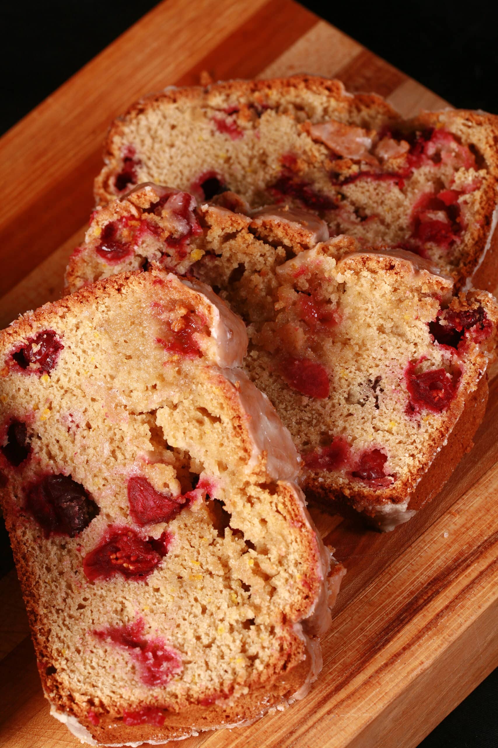 A loaf of glazed gluten-free cranberry orange bread, sliced on a cutting board.