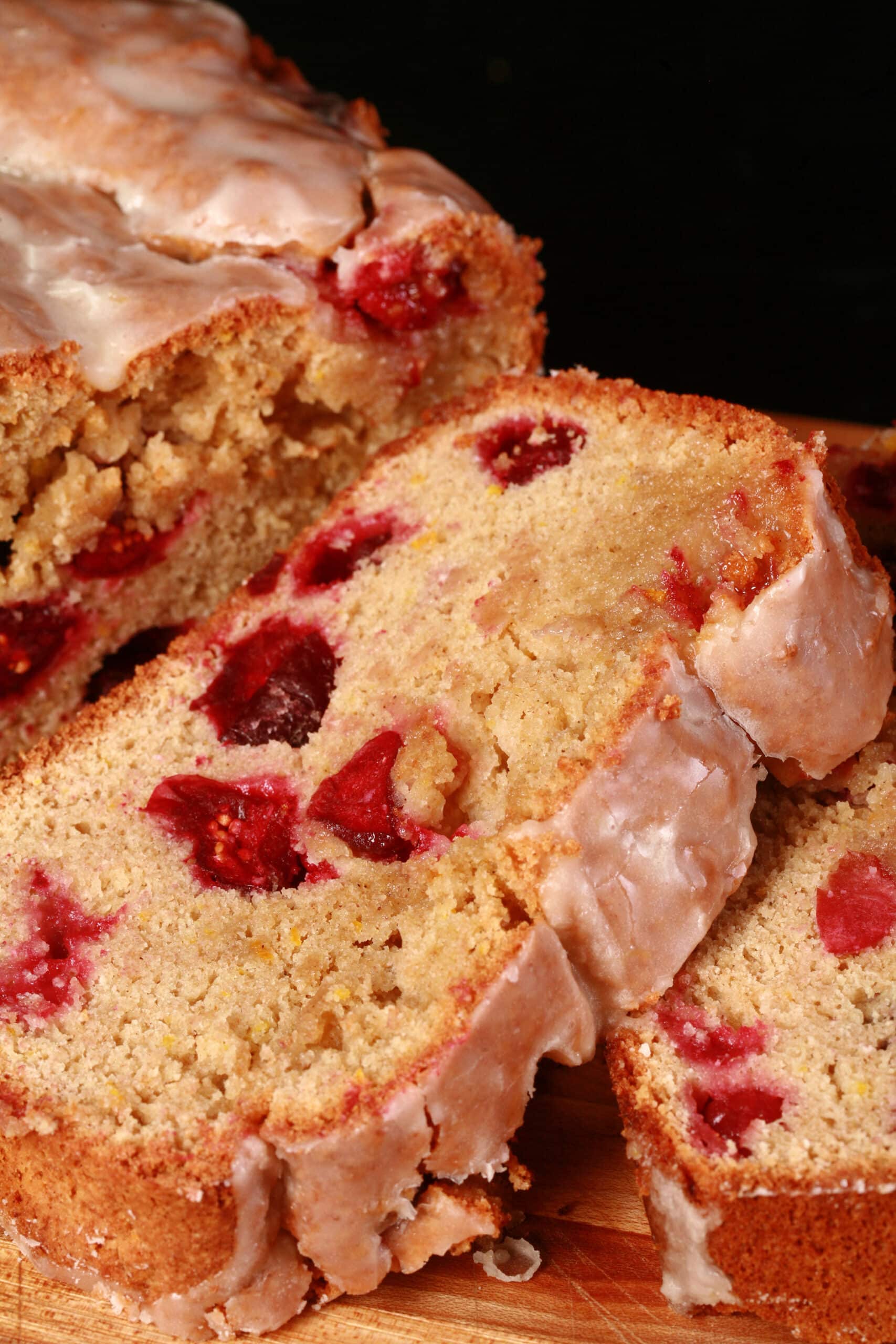 A loaf of glazed gluten free cranberry orange bread, sliced on a cutting board.