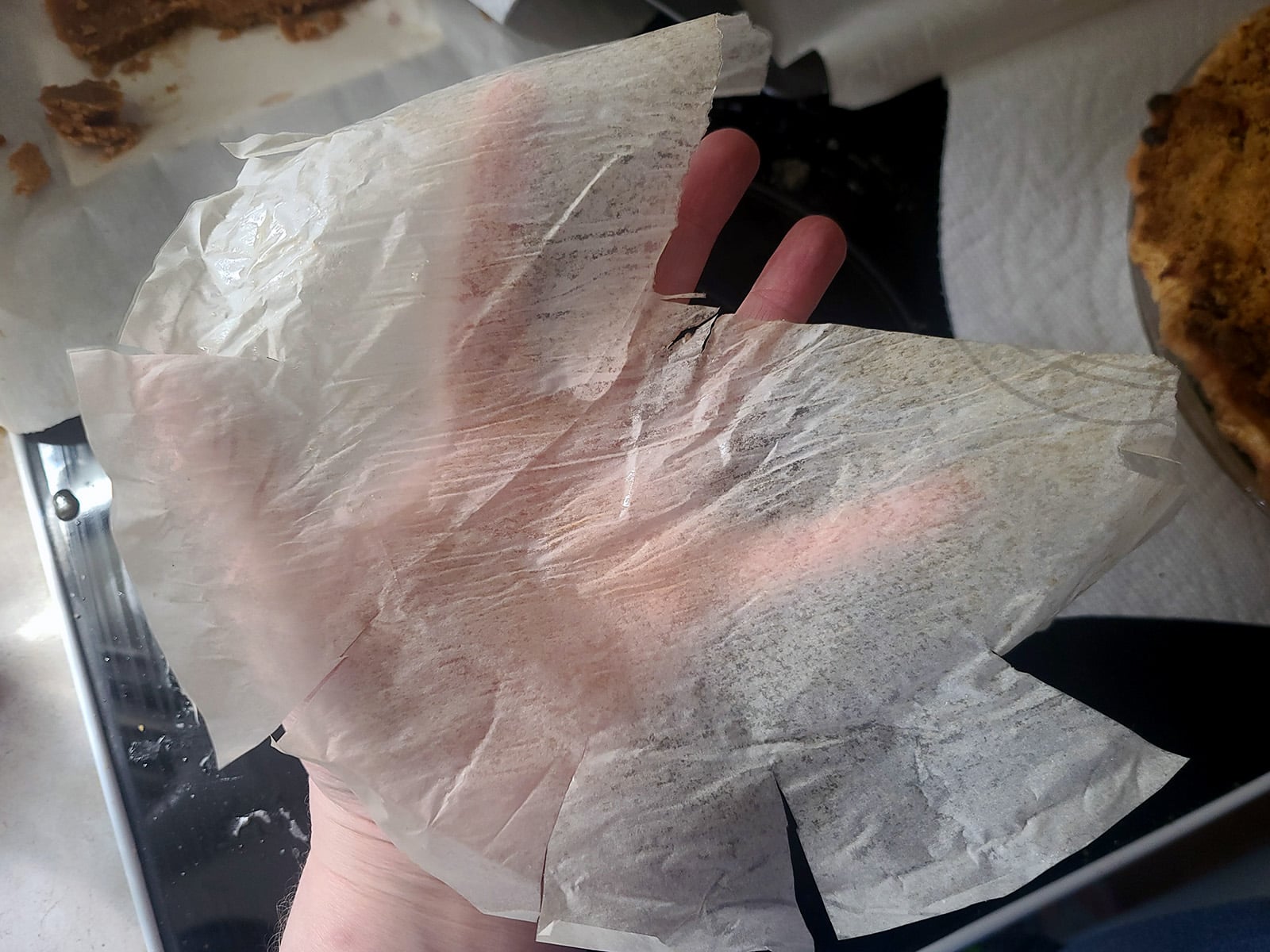 A hand holds the baked round of parchment paper, pulled out from under the baked pie.