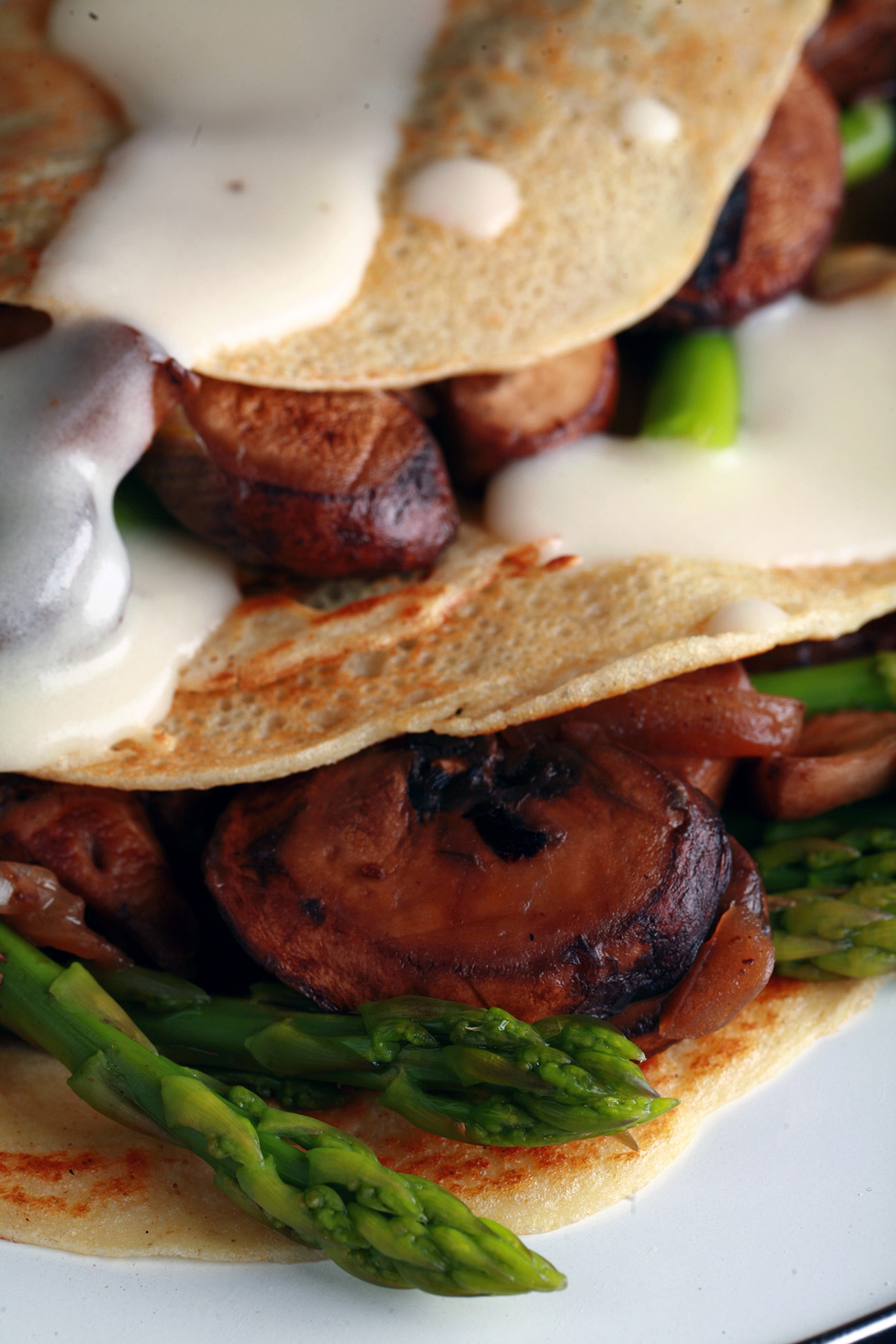 Two gluten free crepes stuffed with mushrooms and aspagus, drizzled with Swiss cheese sauce.