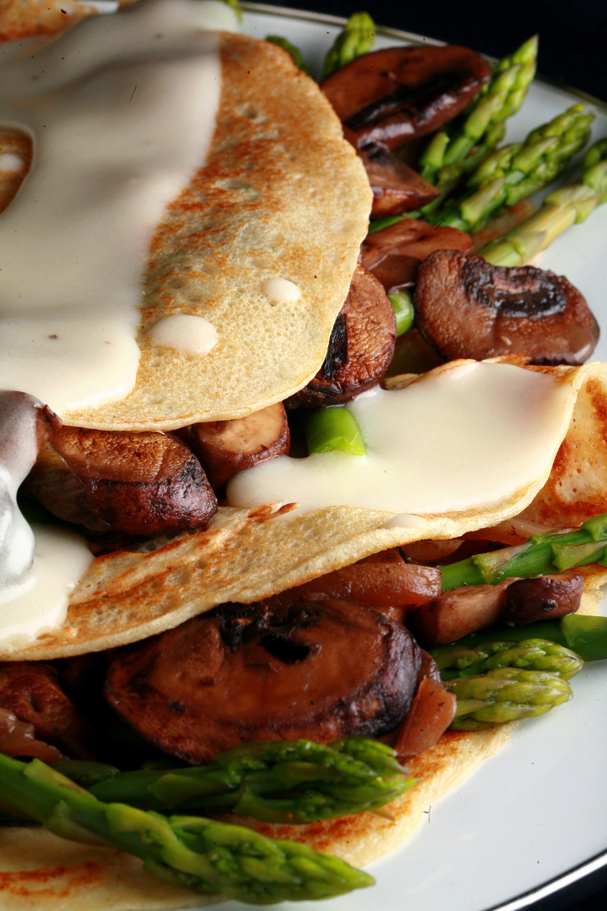 Two gluten free crepes stuffed with mushrooms and aspagus, drizzled with Swiss cheese sauce.