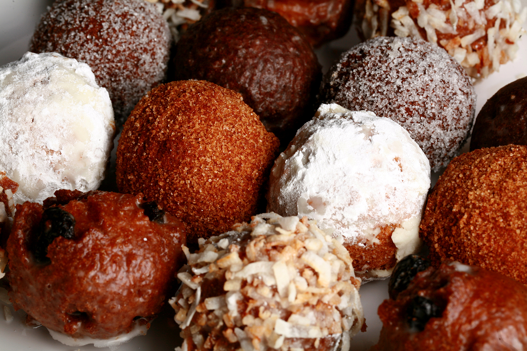 A close up view of an assortment of gluten-free donut holes: Toasted coconut, chocolate glazed, cinnamon sugar, powdered sugar, and dutchie versions are all visible.