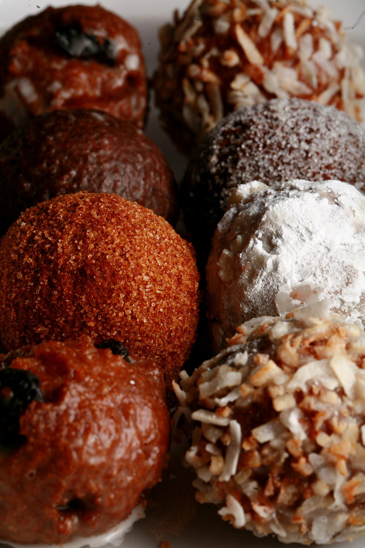 A close up view of an assortment of gluten-free doughnut holes: Toasted coconut, chocolate glazed, cinnamon sugar, powdered sugar, and dutchie versions are all visible.