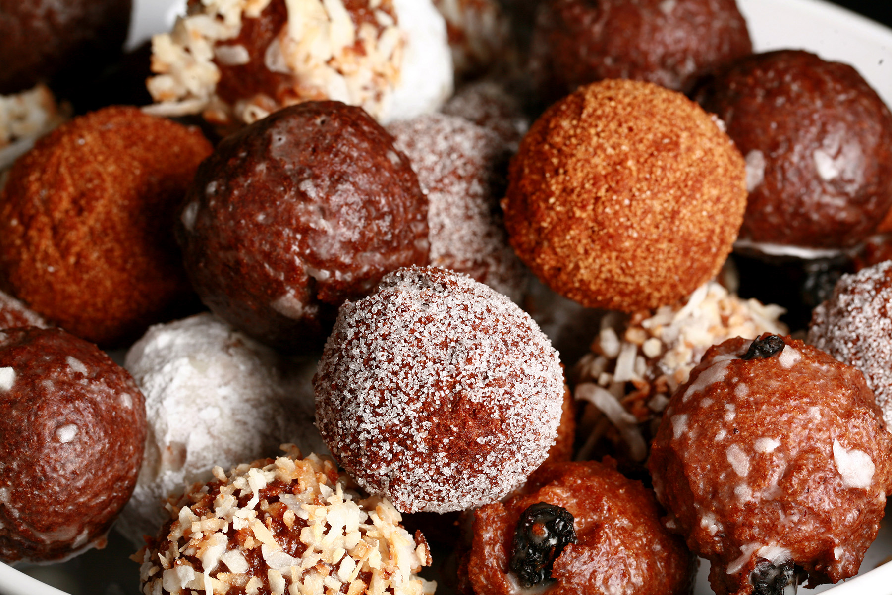 A close up view of an assortment of gluten-free timbits: Toasted coconut, chocolate glazed, cinnamon sugar, powdered sugar, and dutchie versions are all visible.
