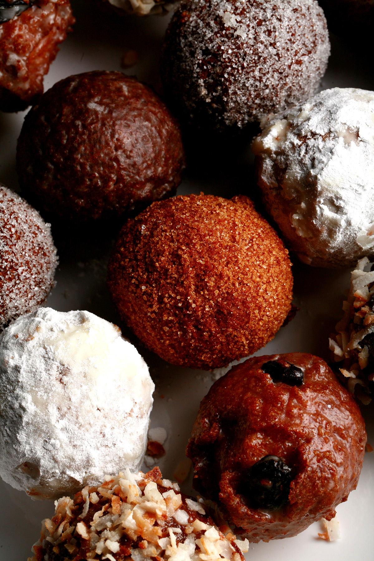 A close up view of an assortment of gluten-free donut holes: Toasted coconut, chocolate glazed, cinnamon sugar, powdered sugar, and dutchie versions are all visible.