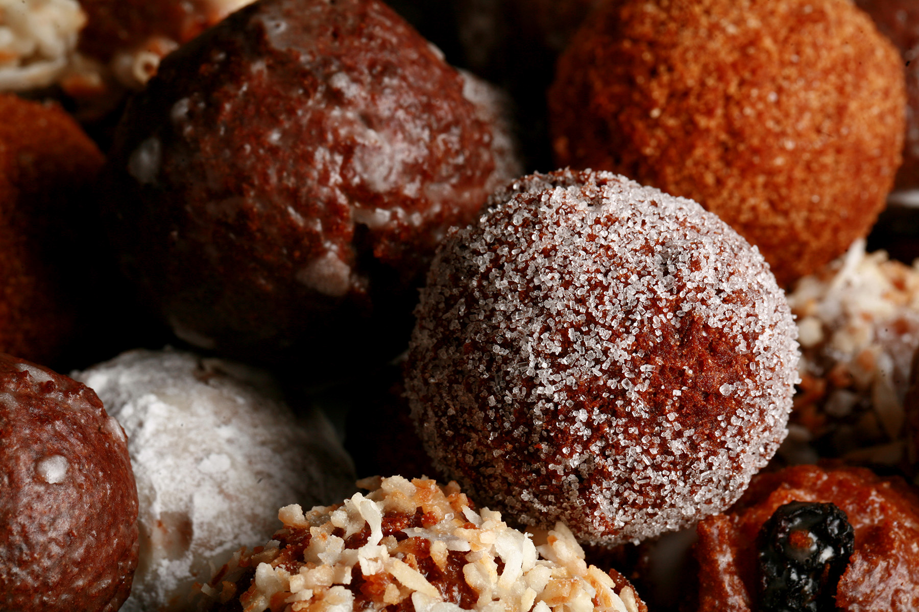 A close up view of an assortment of gluten-free donut holes: Toasted coconut, chocolate glazed, cinnamon sugar, powdered sugar, and dutchie versions are all visible.