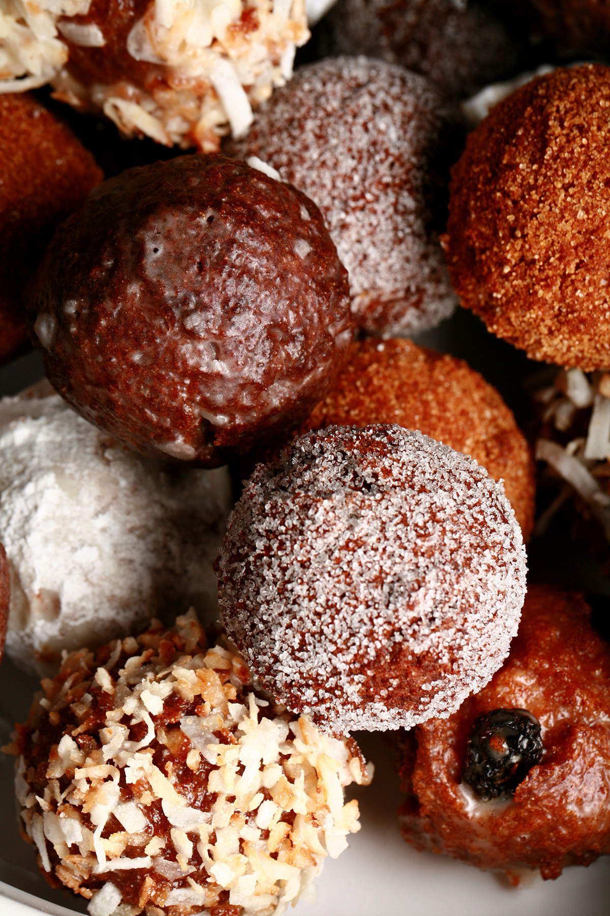 A close up view of an assortment of gluten-free doughnut holes: Toasted coconut, chocolate glazed, cinnamon sugar, powdered sugar, and dutchie versions are all visible.