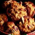 A festive green and red holiday container is full of cookies. The cookies have visible pieces of fruits and nuts throughout.
