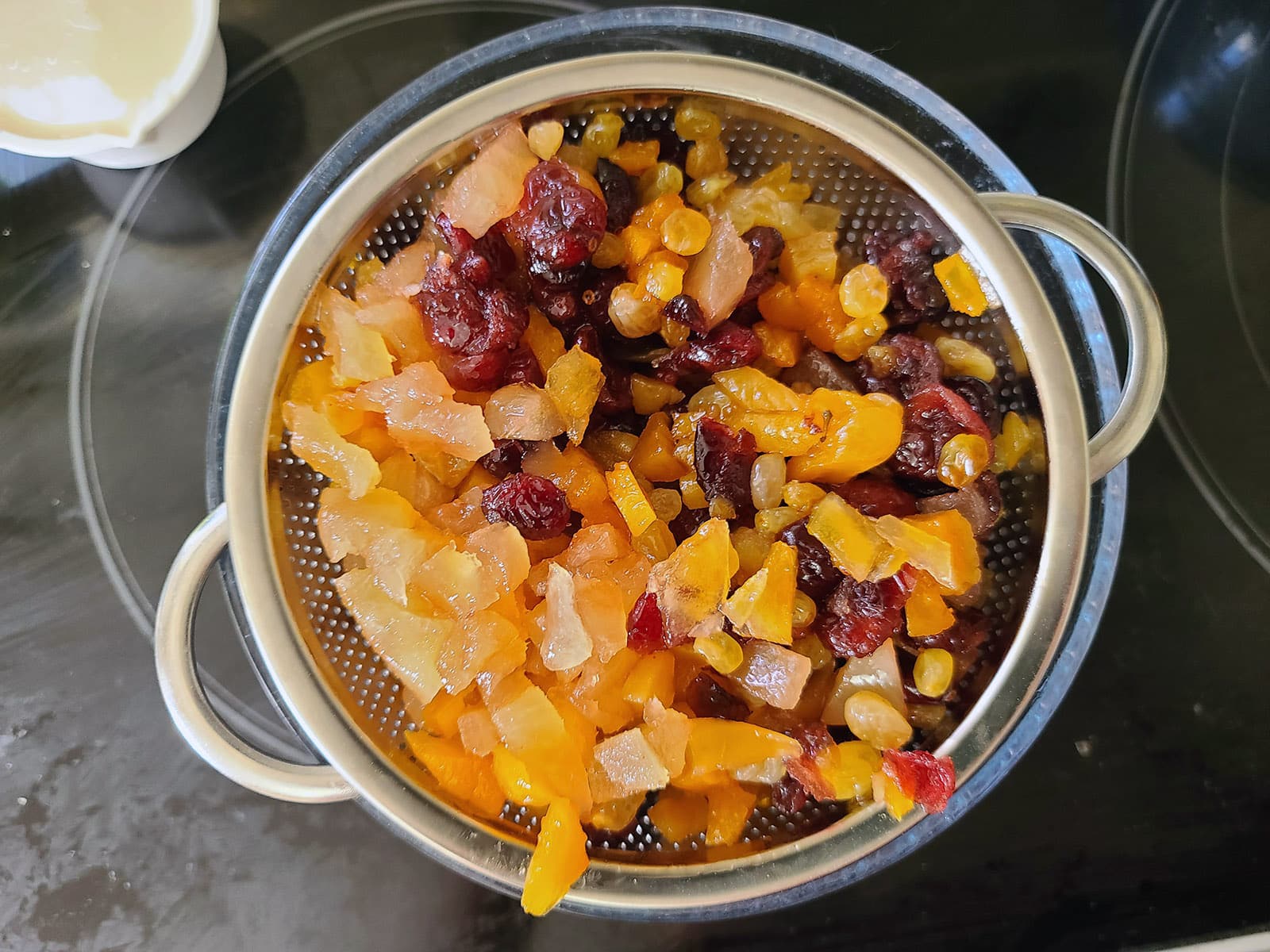 The soaked dried fruit being drained in a wire colander over a bowl.
