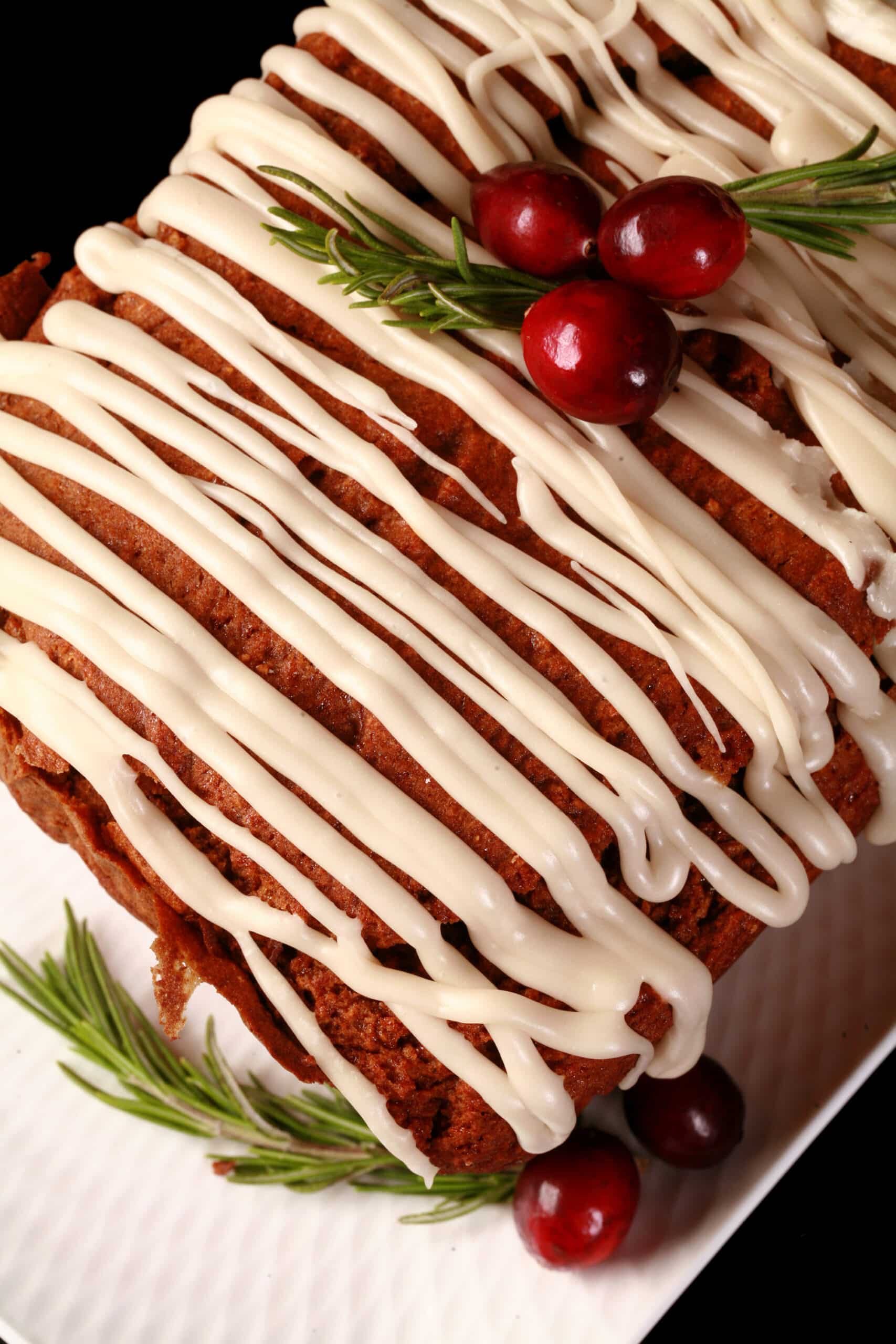 A loaf of gluten free gingerbread loaf, drizzled with vanilla glaze and garnished with rosemary and cranberries.
