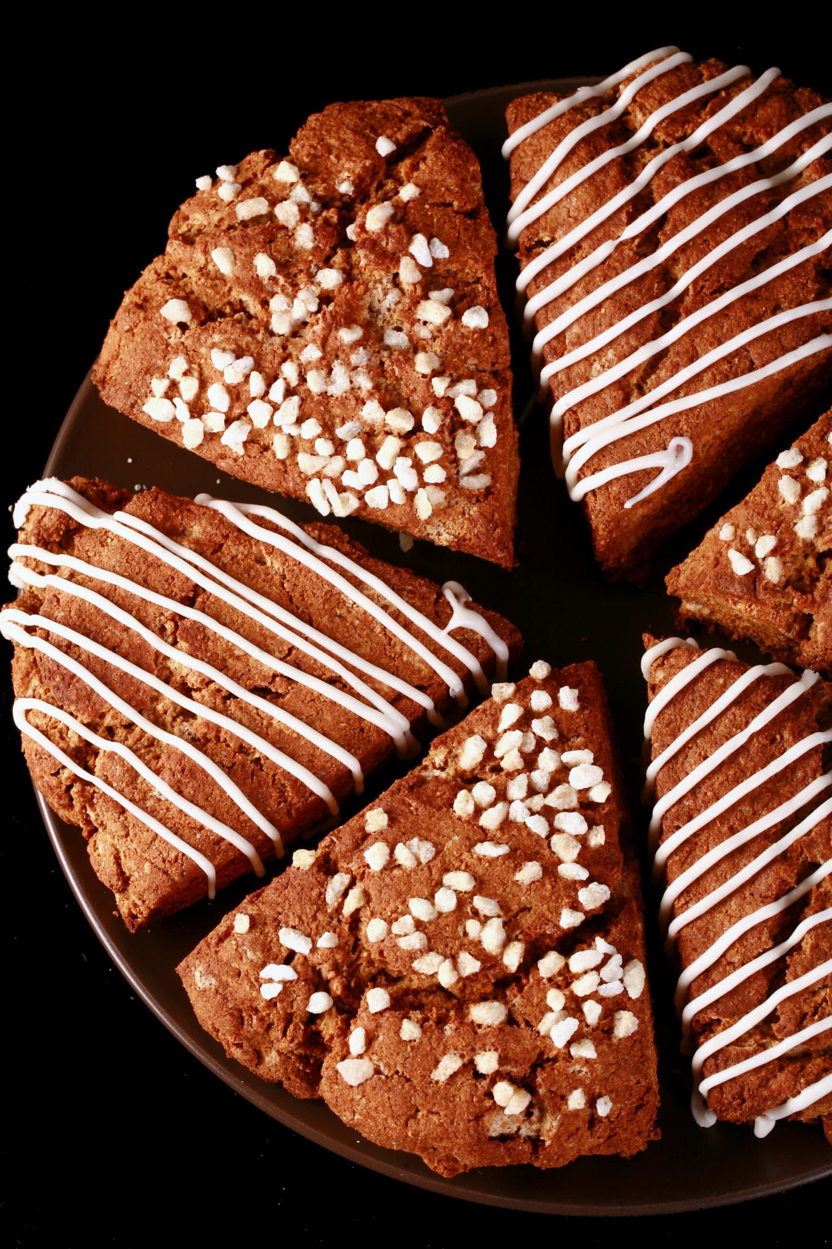 A plate of gluten free gingerbread scones. Half have a sugar crust, the other half have a vanilla glaze drizzled over them.