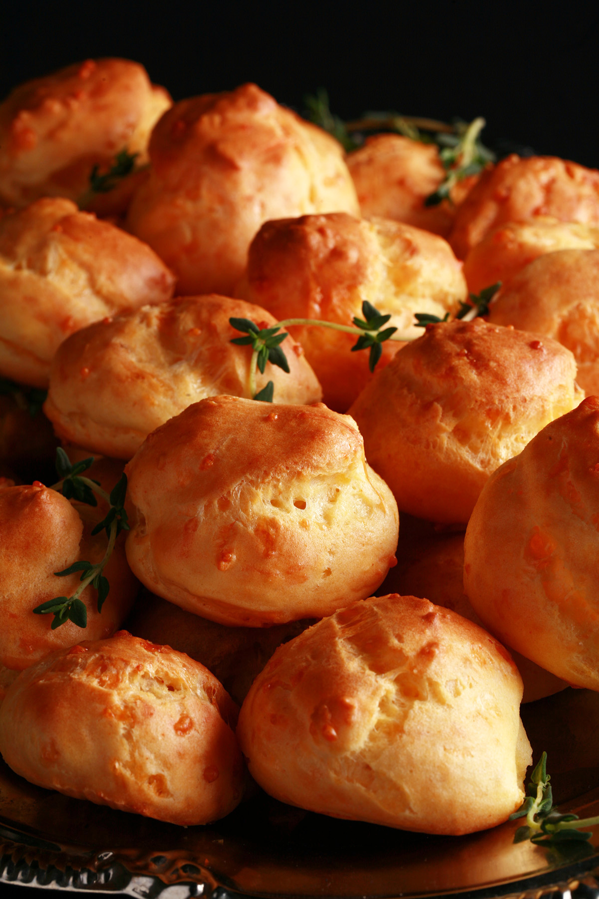 A large pile of Gluten-free Gougères - small, cheesy pastries - on a silver plate.
