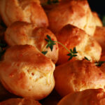 A large pile of Gluten-free Cheese Puffs - small, cheesy pastries - on a silver plate.