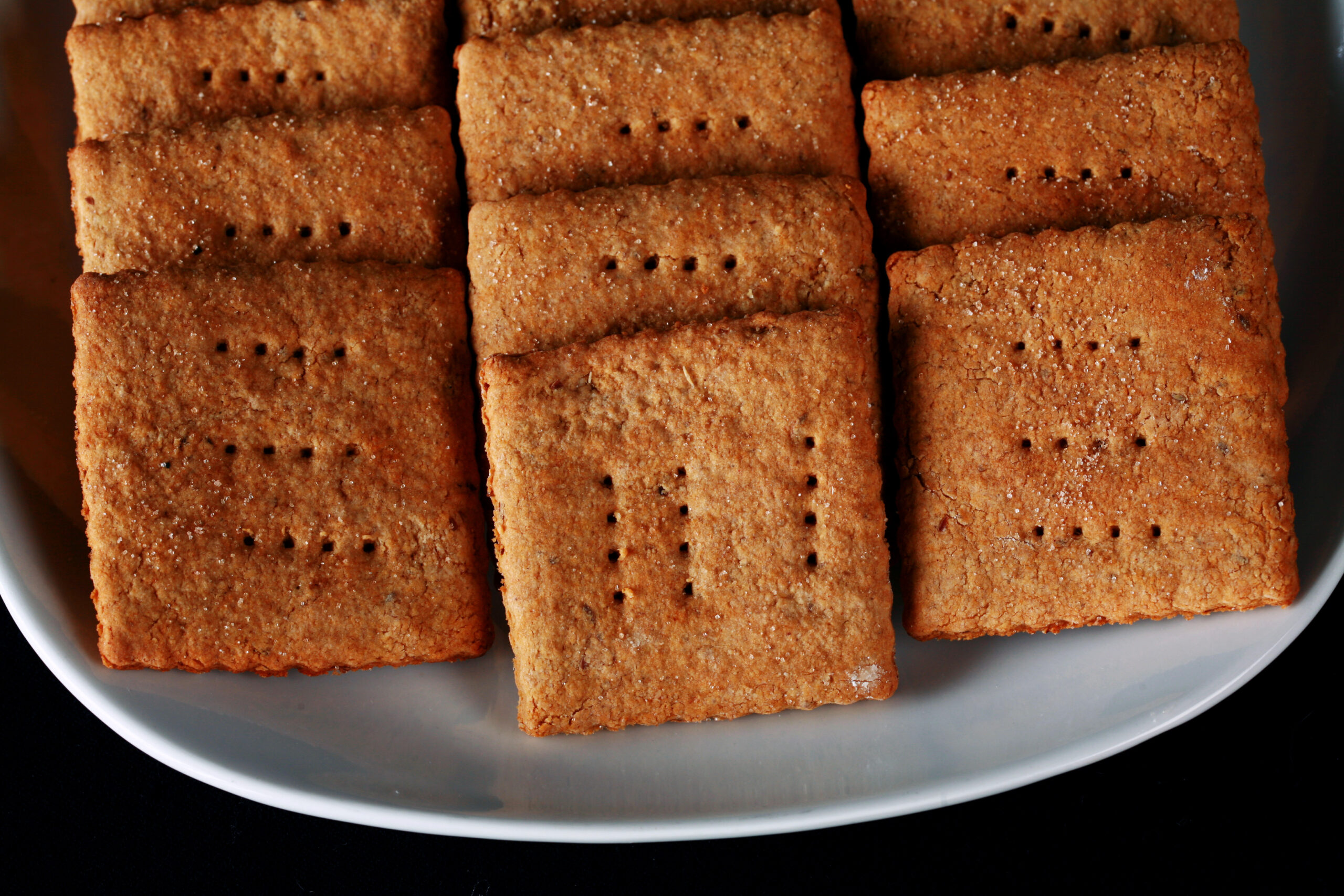 A white plate with rows of square shaped gluten-free graham crackers.