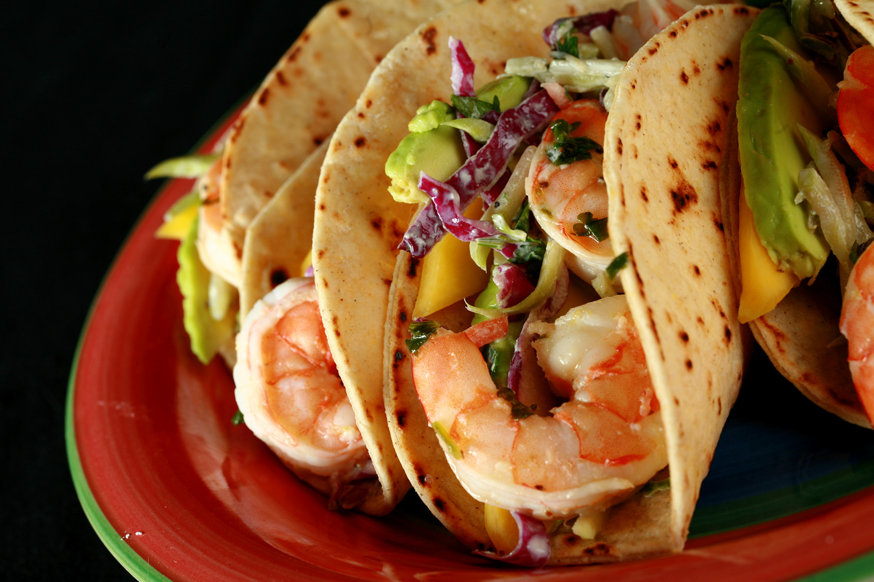 A red plate with shrimp tacos. The tacos are made from gluten-free hybrid tortillas, and look like a more yellow version of flour tortillas.
