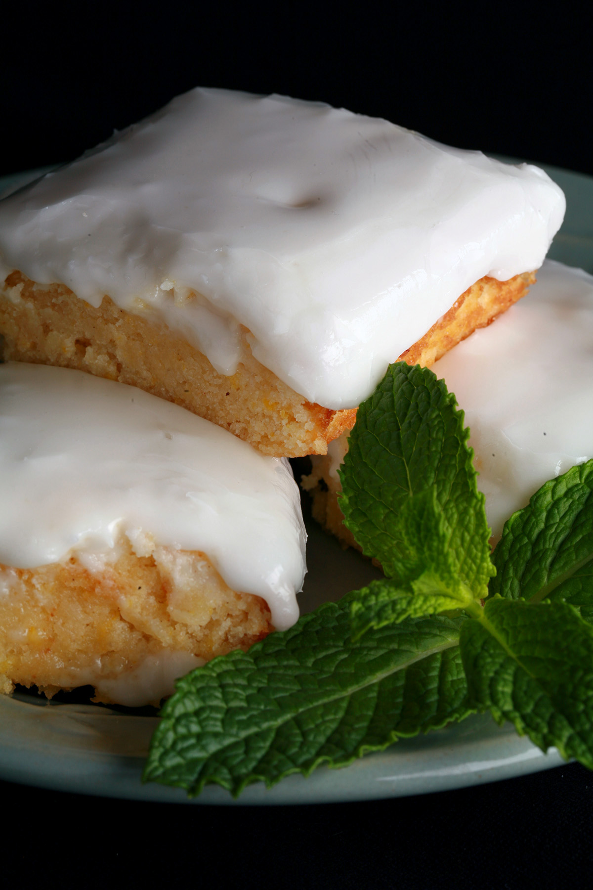 A plate of frosted chewy gluten free lemon bars, garnished with mint leaves.