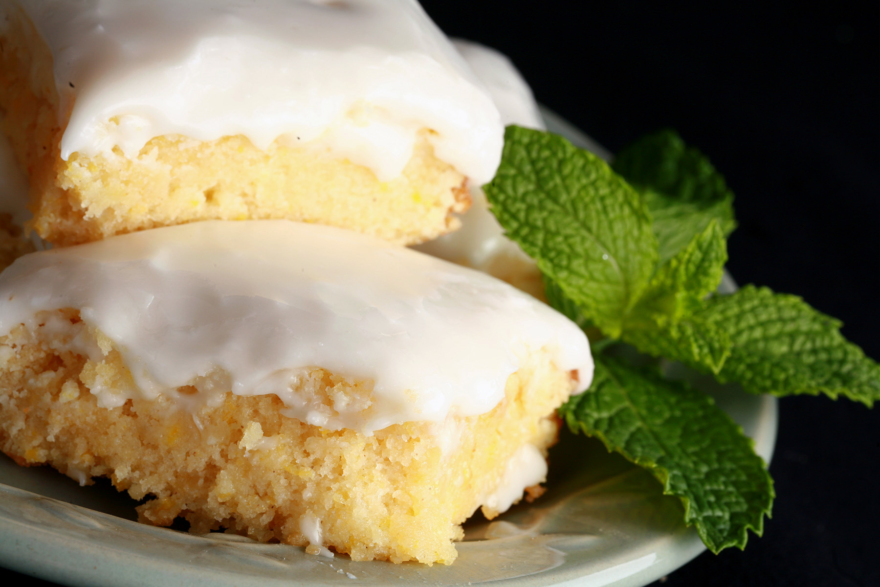 A plate of frosted chewy gluten free lemon bars, garnished with mint leaves.