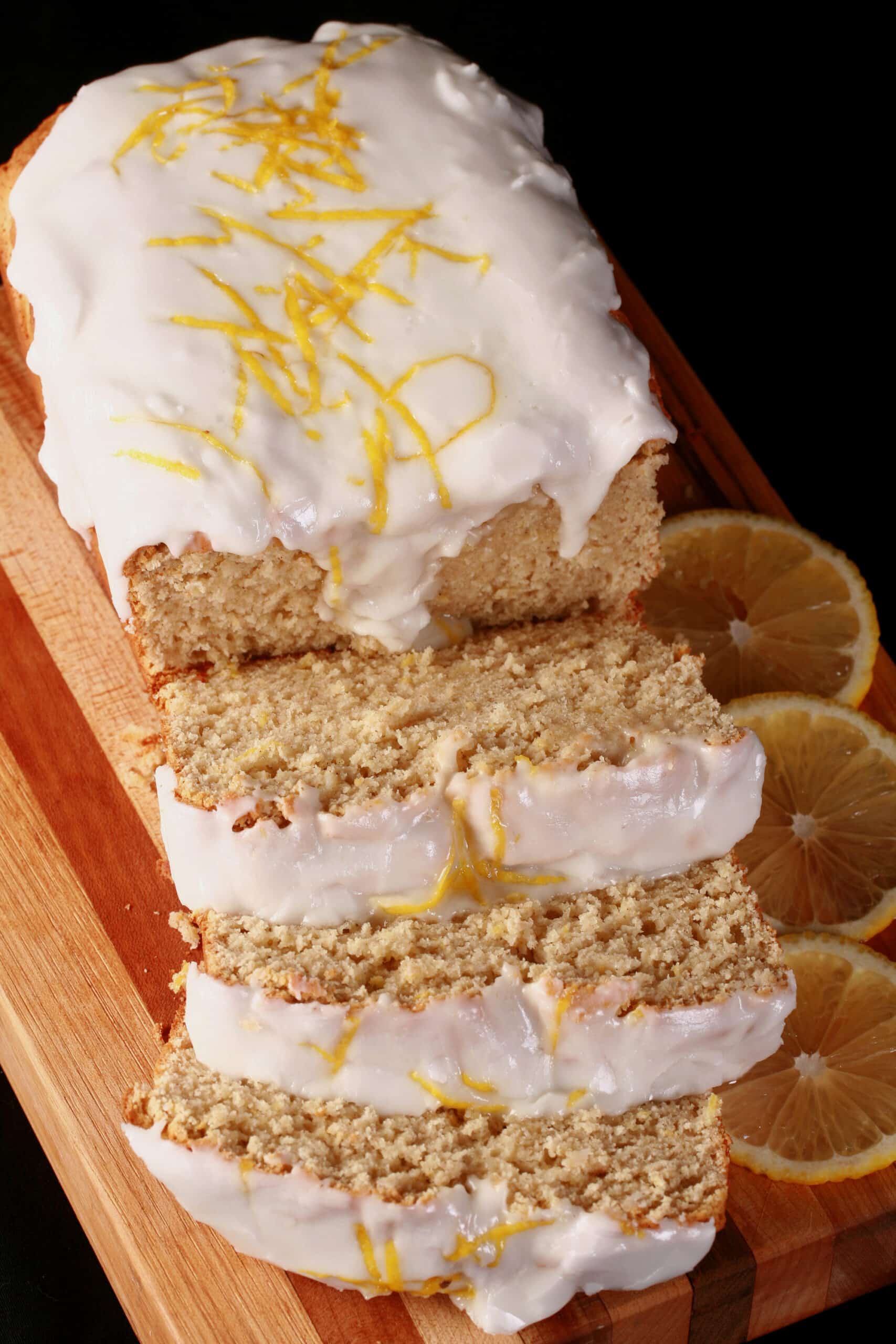 A sliced loaf of gluten free lemon loaf, with white glaze and lemon zest on top.