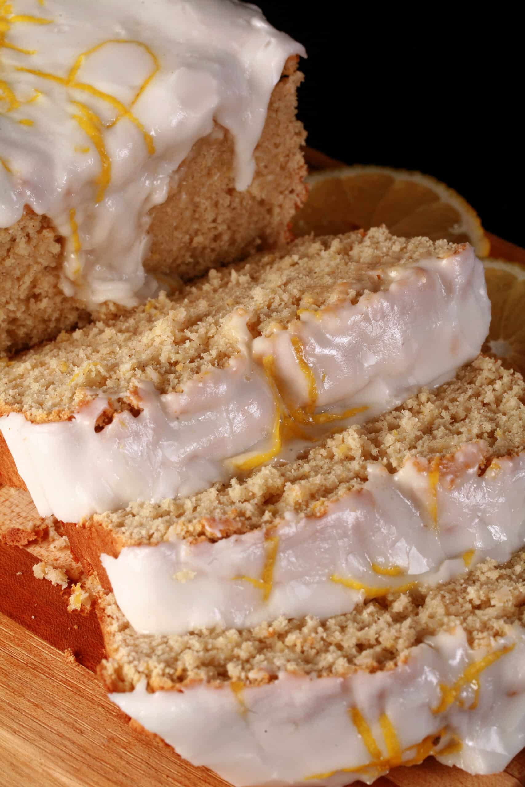 A sliced loaf of gluten free lemon drizzle cake, with white glaze and lemon zest on top.