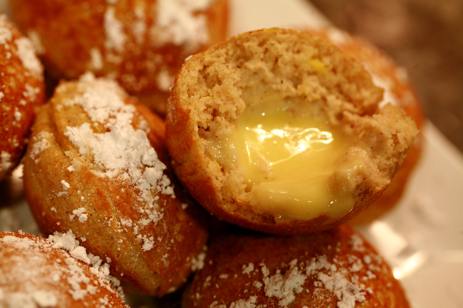 Several gluten-free lemon mascarpone ebelskivers - bite sized stuffed pancakes - on a plate. They're dusted with powdered sugar.
