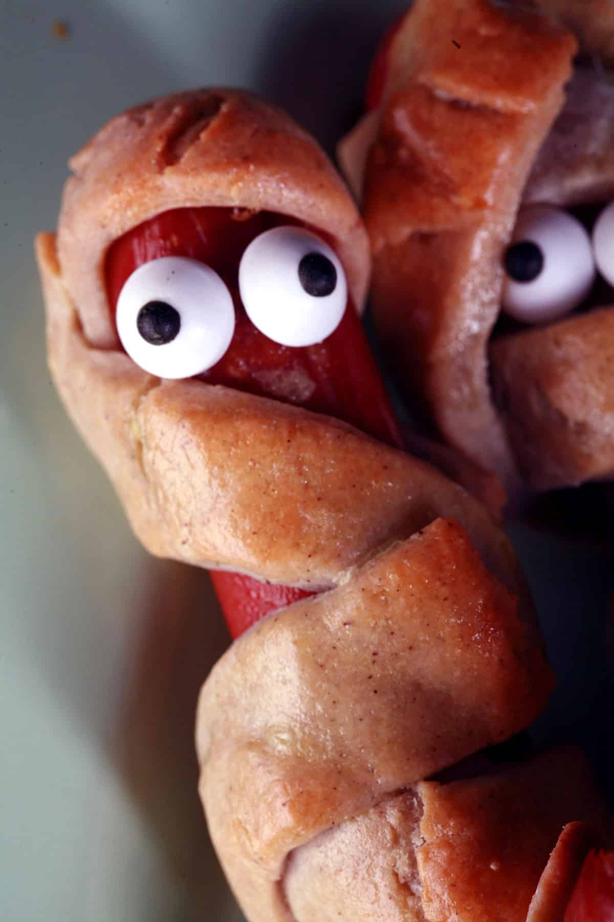 Several gluten free mummy dogs on a plate. Each have 2 candy eyes.