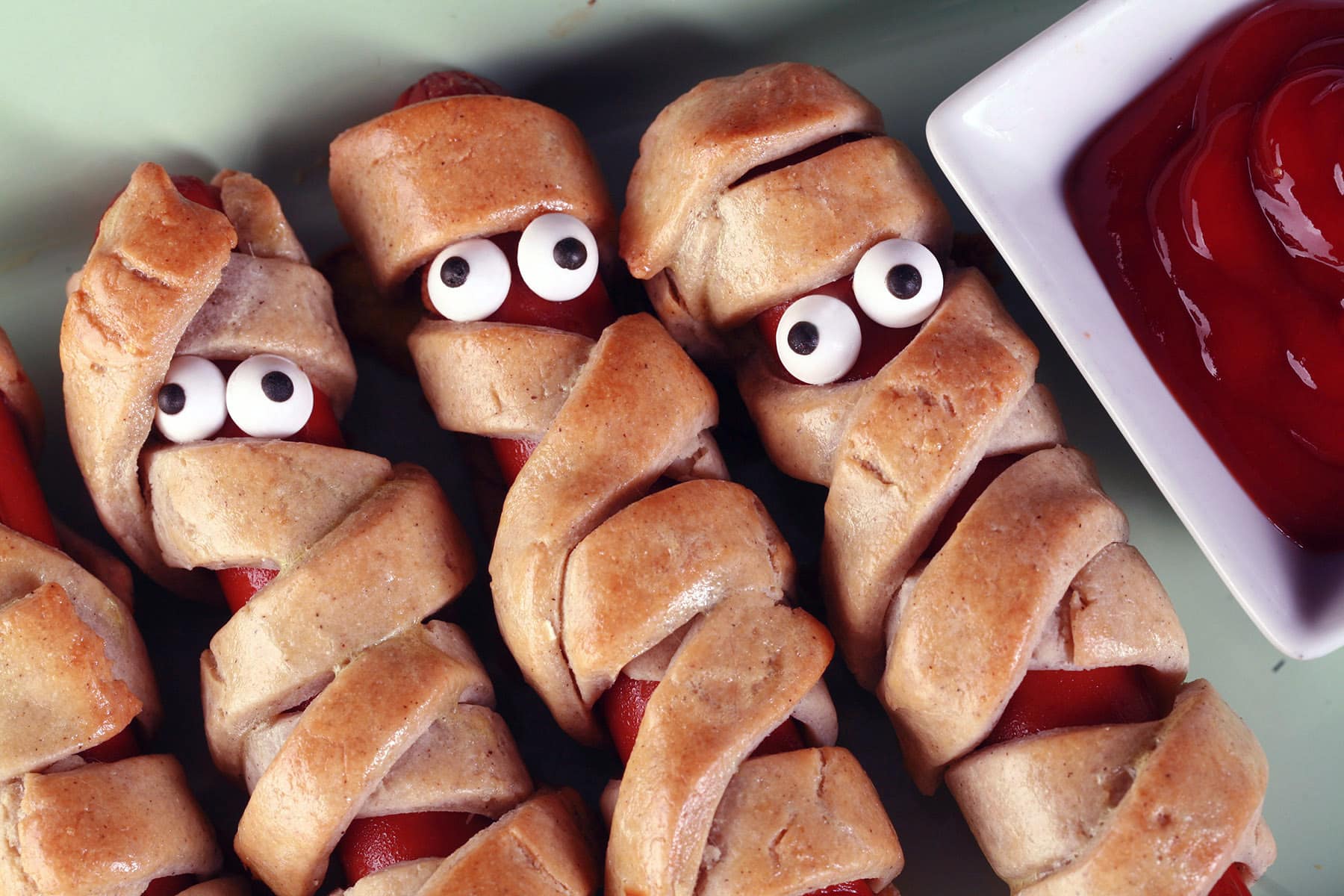 Several gluten free mummy dogs on a plate. Each have 2 candy eyes.