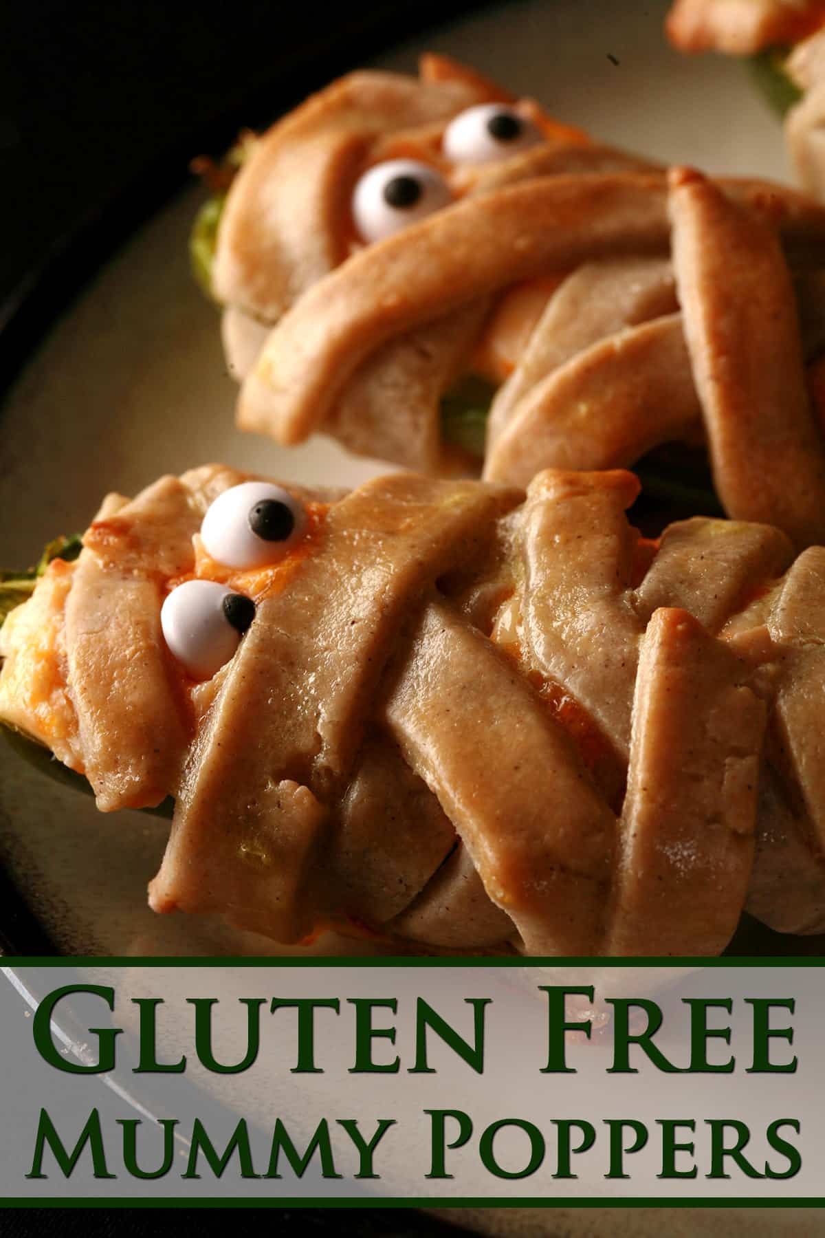 Several gluten free mummy jalapeno poppers on a plate. Each has 2 candy eyeballs.