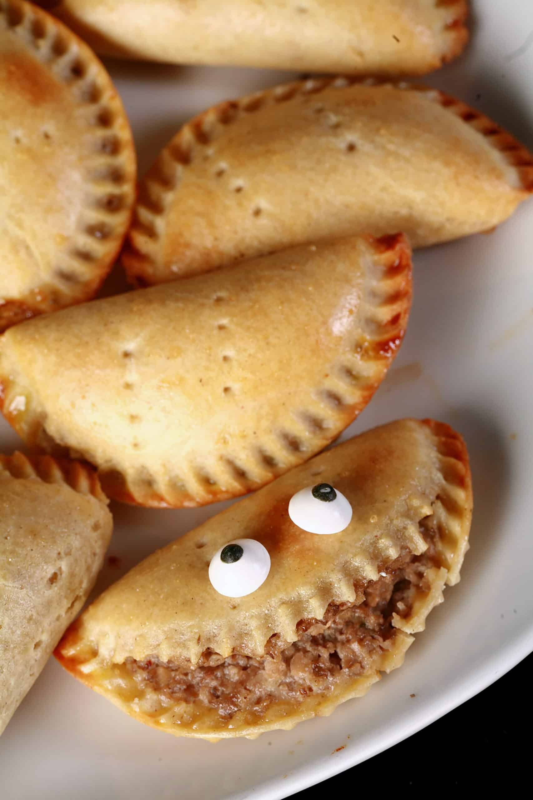 A plate of gluten free mushroom turnovers. One is split open and has candy eyeballs on it, looking like a grinning face.