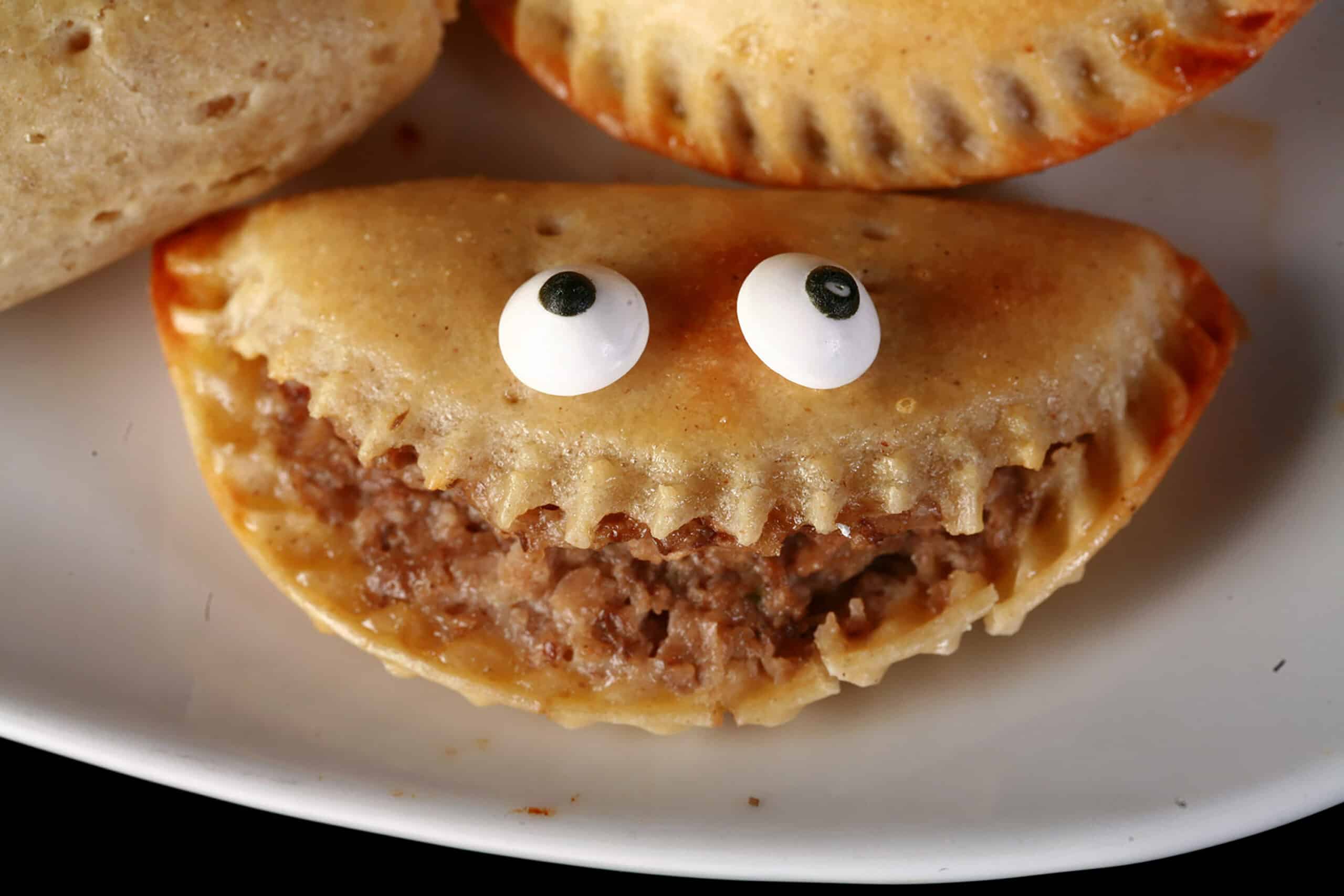 A plate of gluten free mushroom turnovers. One is split open and has candy eyeballs on it, looking like a grinning face.