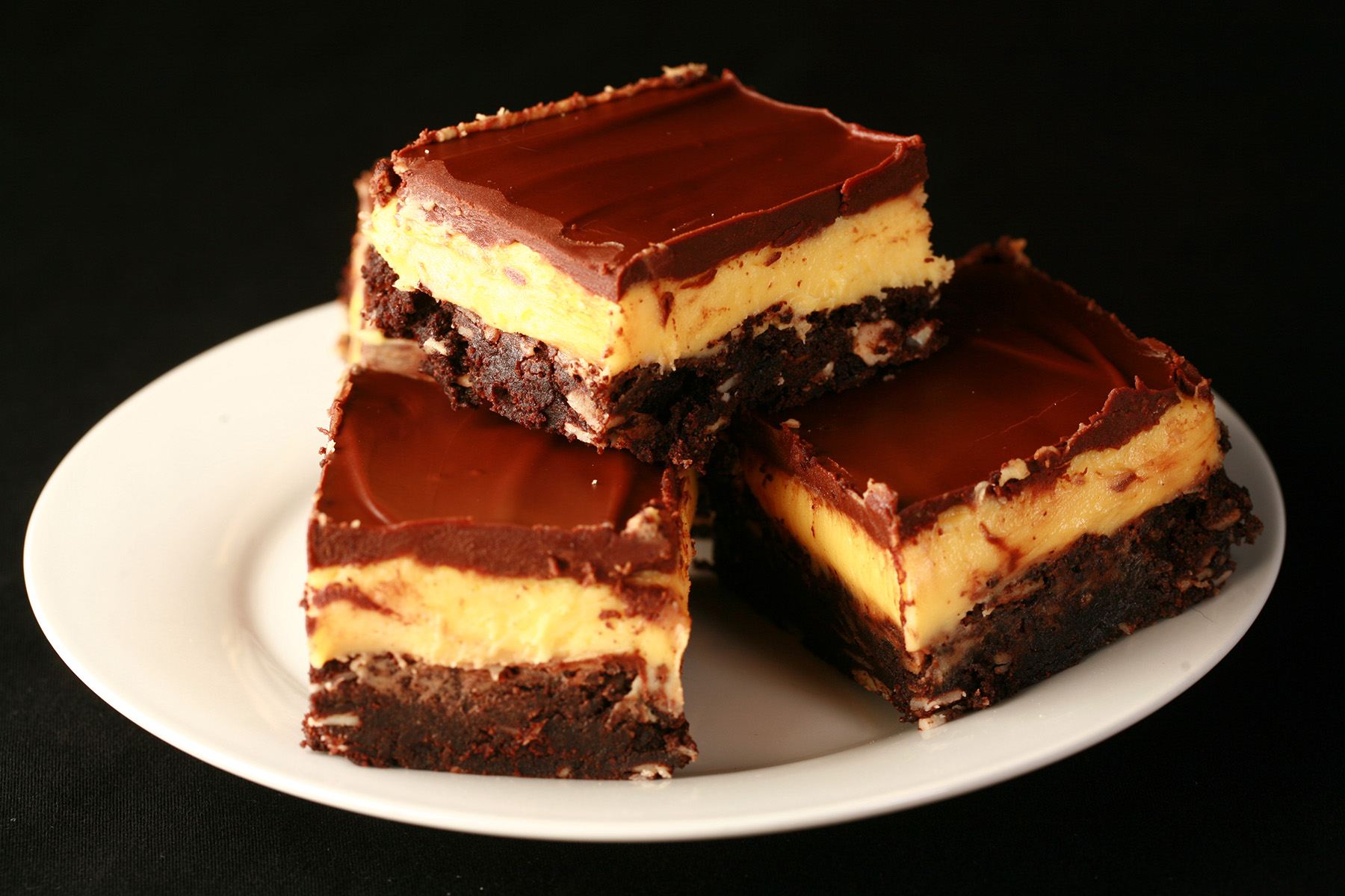 A plate of gluten-free Nanaimo Bars - A fudgey brownie, topped with a rich custard buttercream and a layer of chocolate ganache.