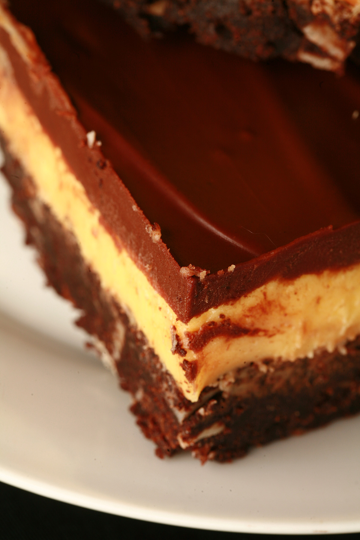 A plate of gluten-free Nanaimo Bar Brownies - A fudgey brownie, topped with a rich custard buttercream and a layer of chocolate ganache.