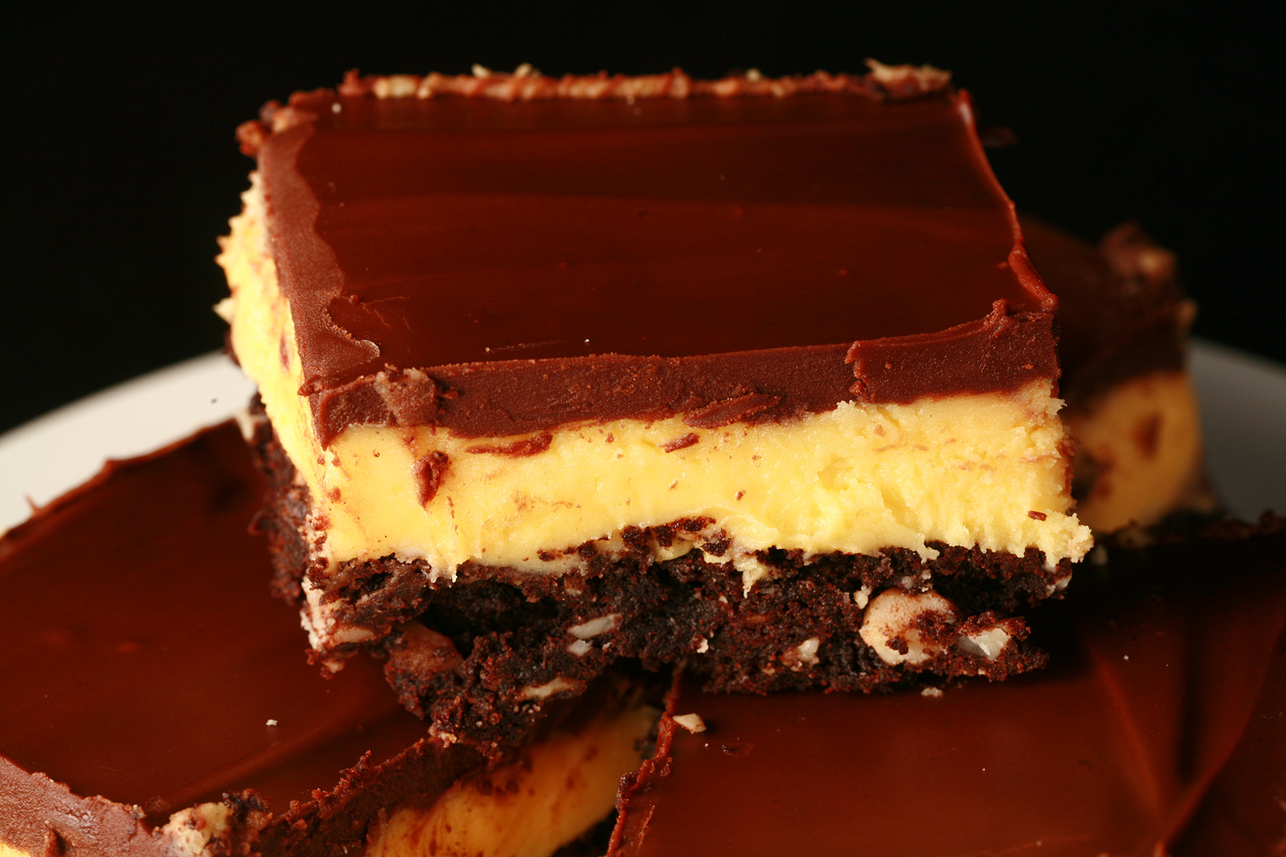 A plate of gluten-free Nanaimo Bars - A fudgey brownie, topped with a rich custard buttercream and a layer of chocolate ganache.