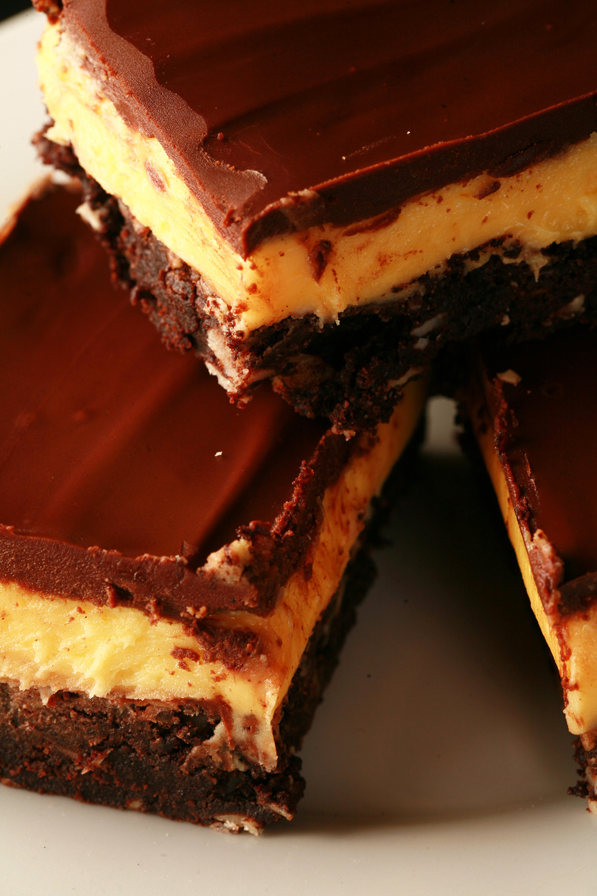 A plate of gluten-free Nanaimo Bar Brownies - A fudgey brownie, topped with a rich custard buttercream and a layer of chocolate ganache.