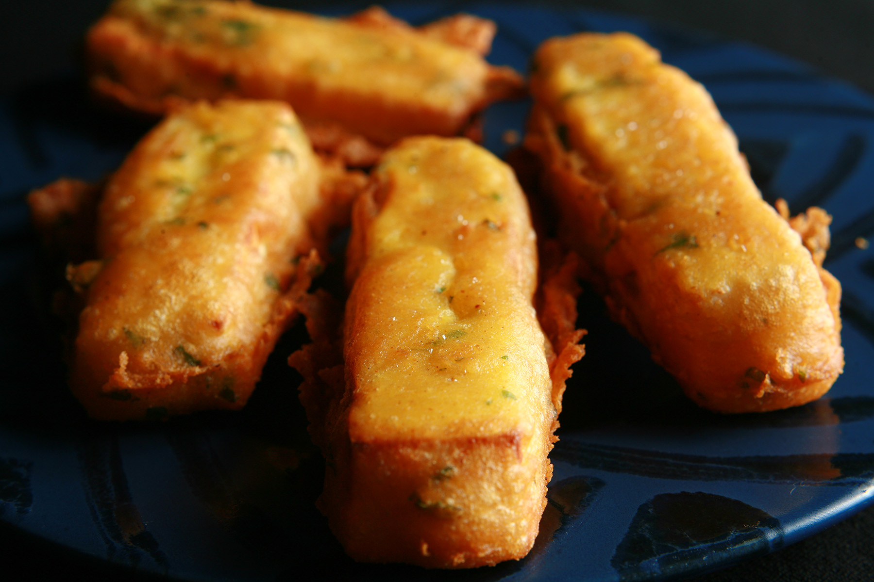 Several sticks of gluten-free paneer pakora - deep fried cheese sticks - on a blue plate.