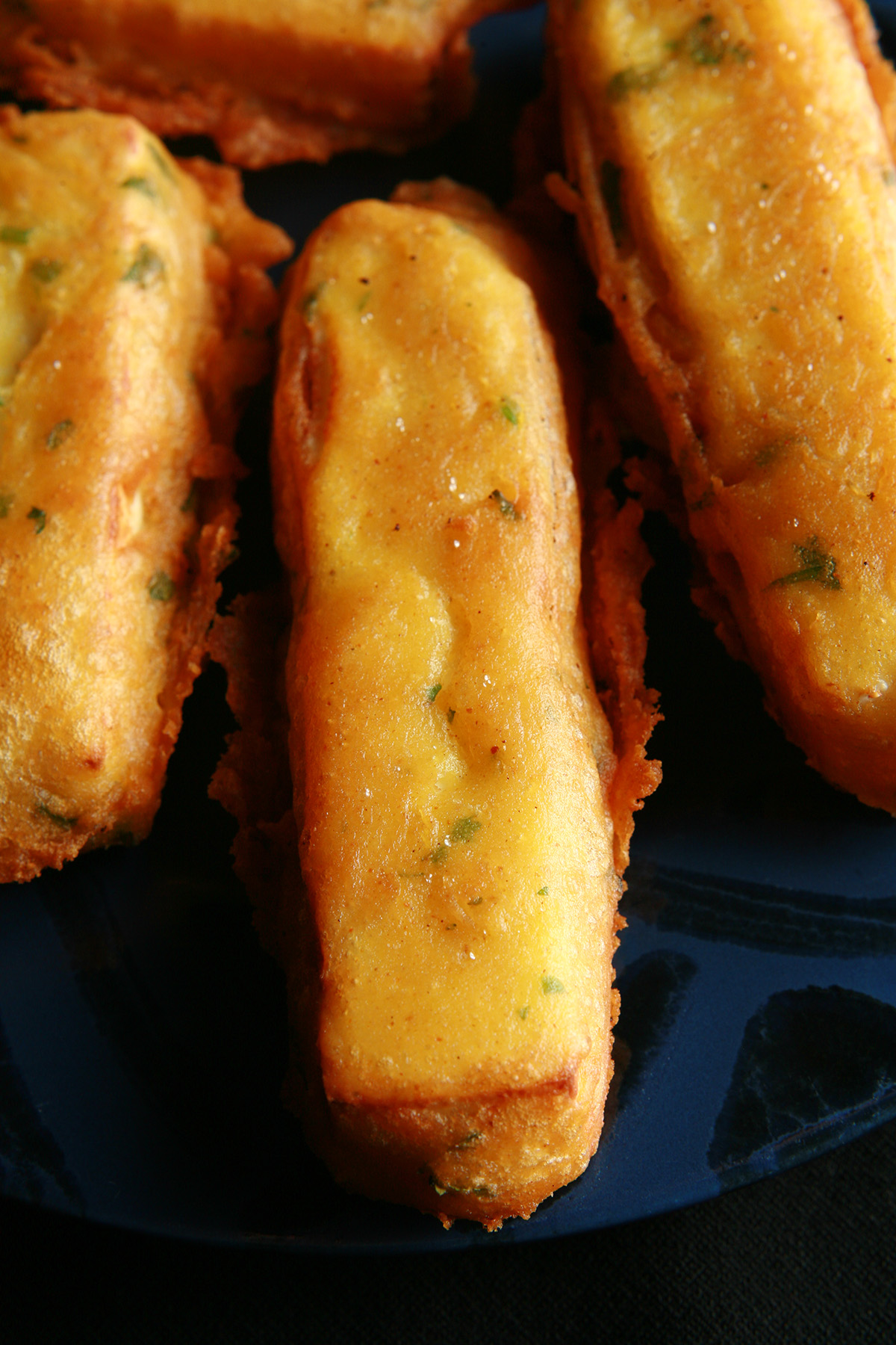 Several sticks of gluten-free paneer pakora - deep fried cheese sticks - on a blue plate.