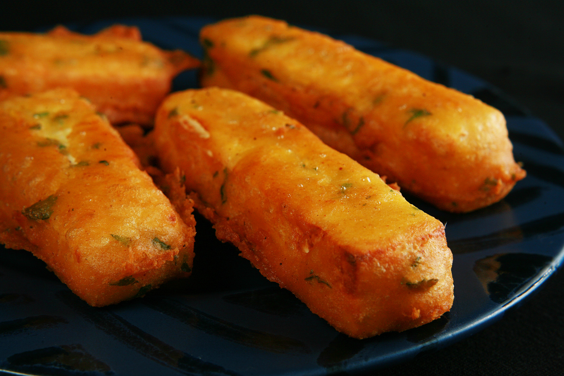 Several sticks of gluten-free paneer pakora - deep fried cheese sticks - on a blue plate.