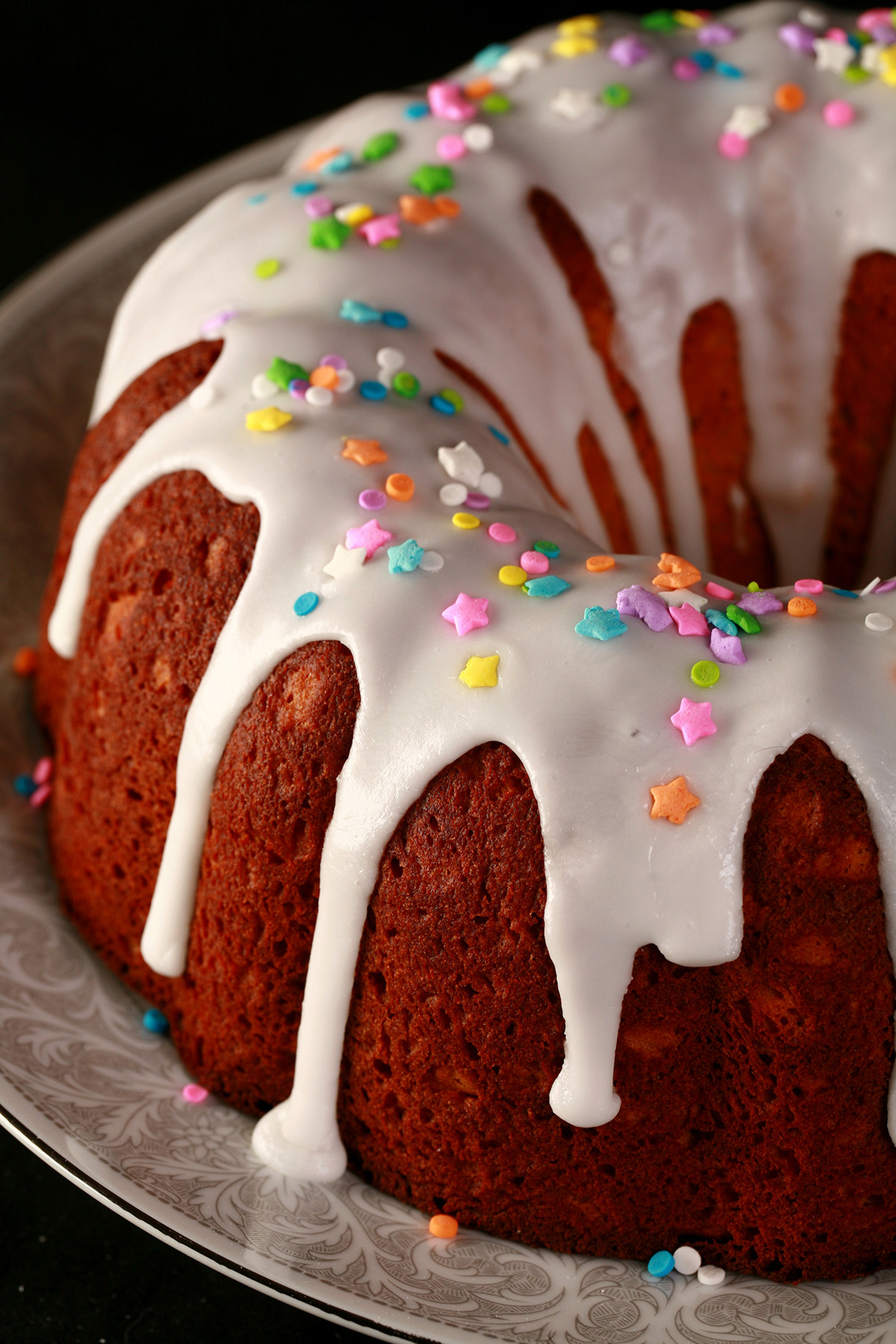 A close up view of a gluten-free paska. It's in the shape of a bundt pan, with dripping white glaze and topped with pastel coloured sprinkles.