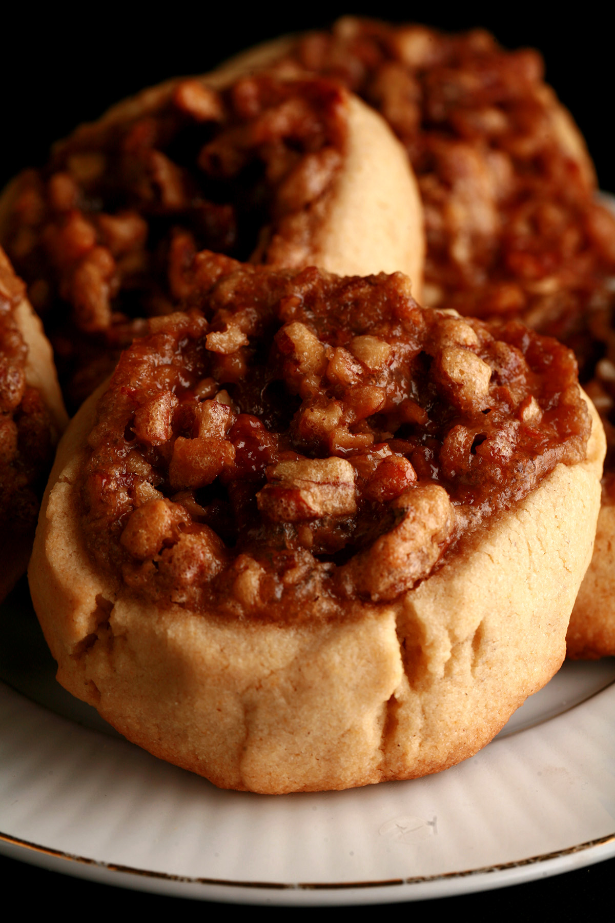 Several Gluten-Free Pecan Pie cookies on a white plate. They are golden brown, with a pecan and brown sugar topping.
