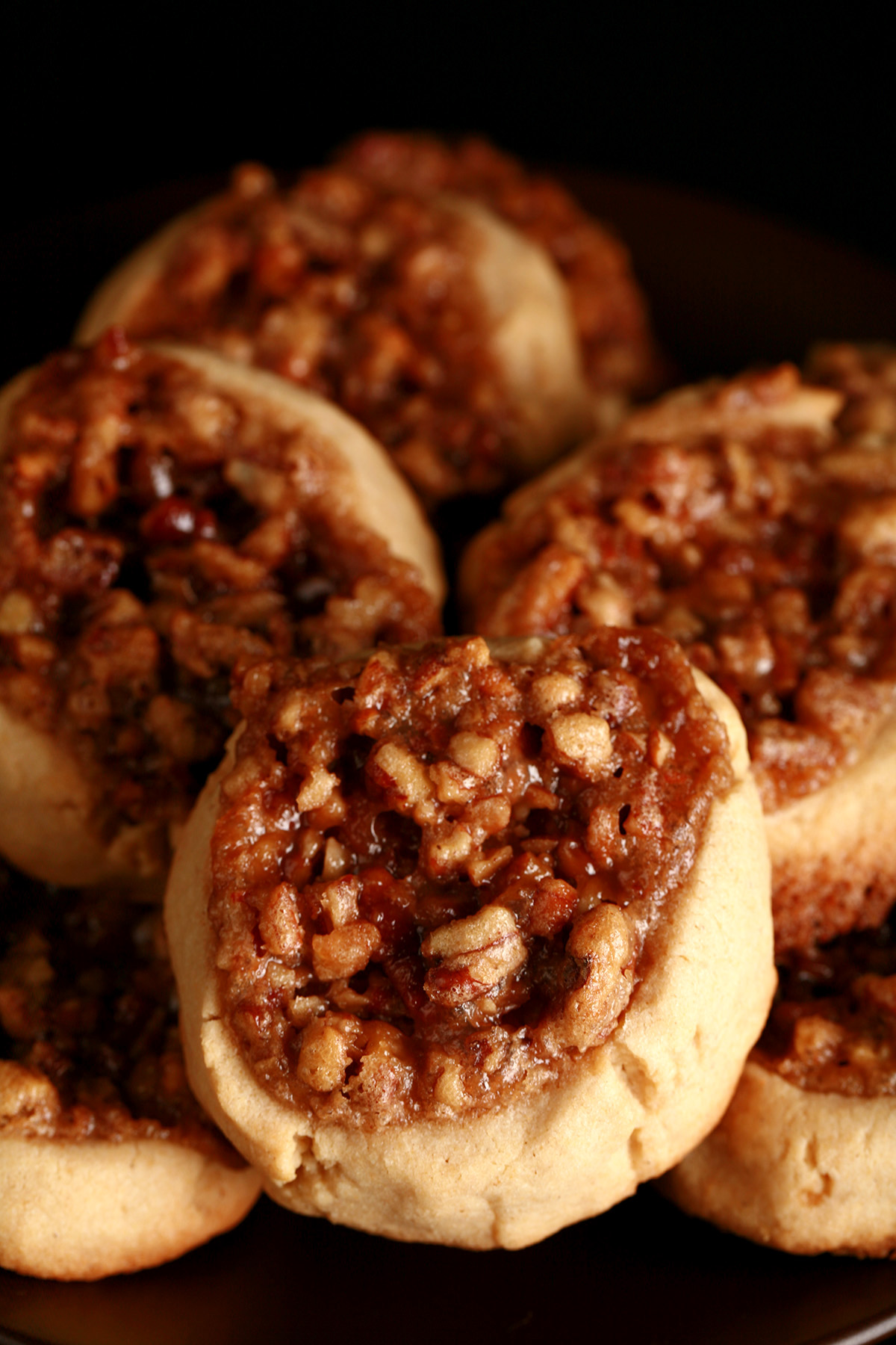 Several Gluten-Free Pecan Pie cookies on a white plate. They are golden brown, with a pecan and brown sugar topping.