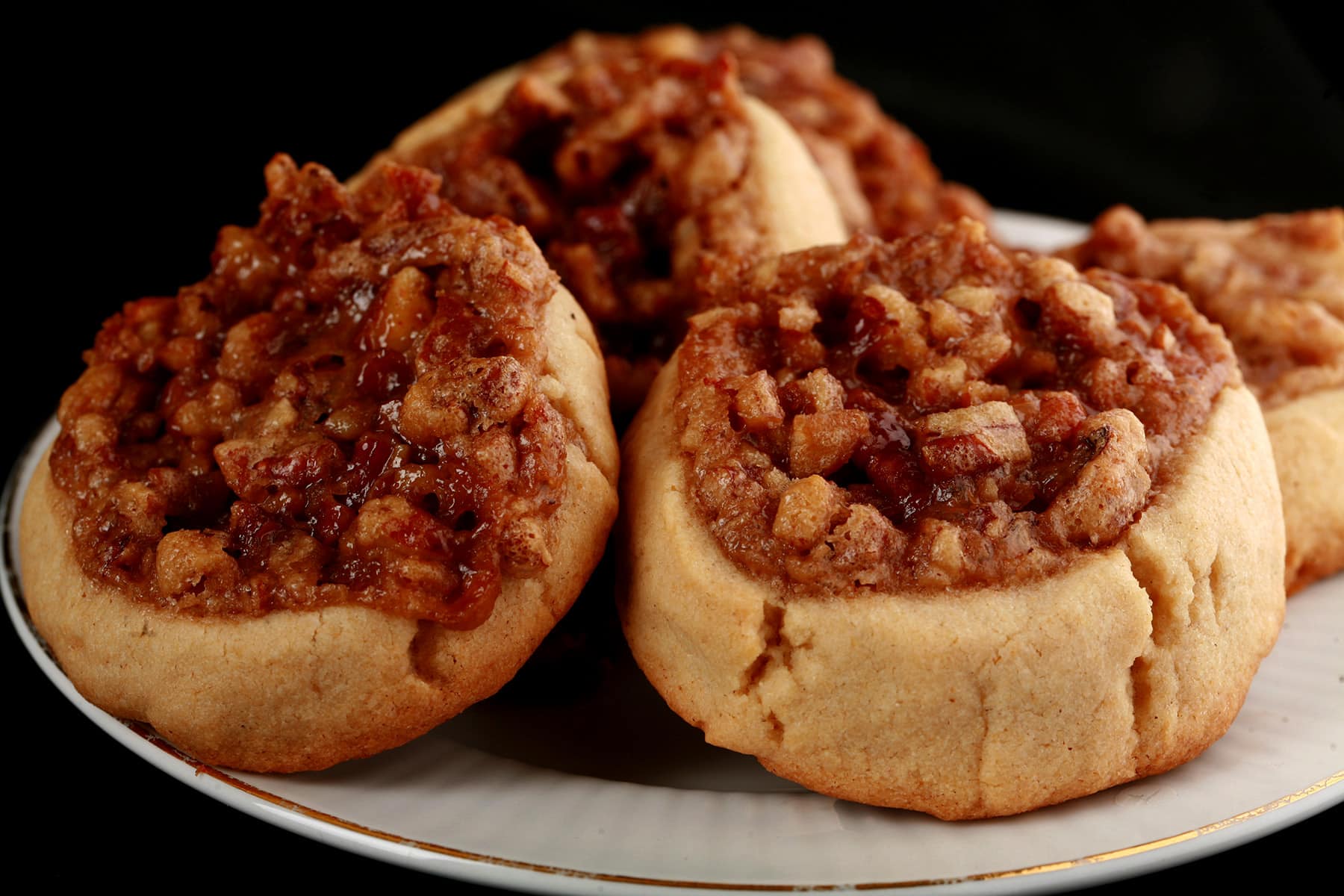 Several Gluten-Free Pecan Pie cookies on a white plate. They are golden brown, with a pecan and brown sugar topping.