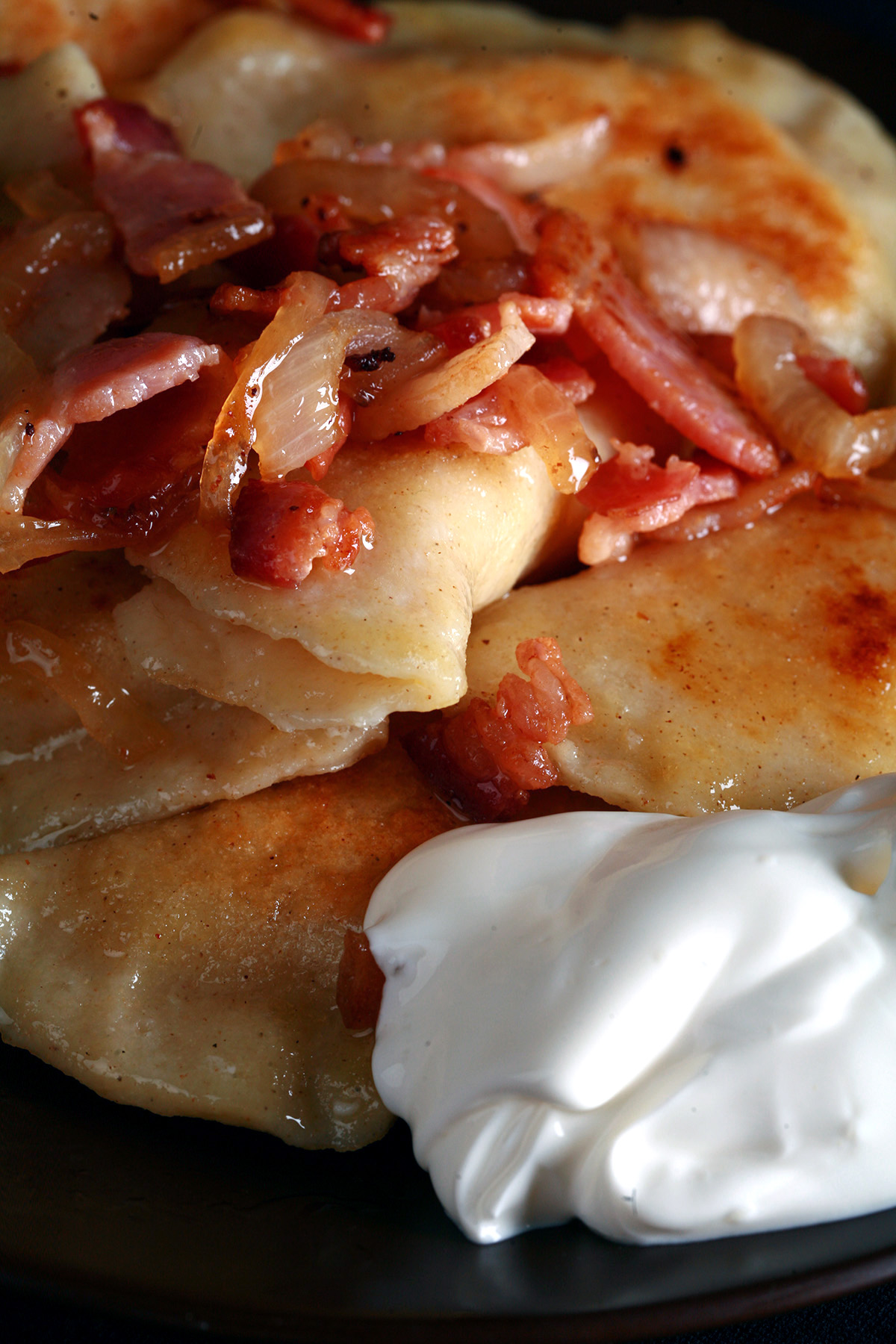 A plate of gluten-free pierogi, topped with bacon, fried onions, and sour cream.