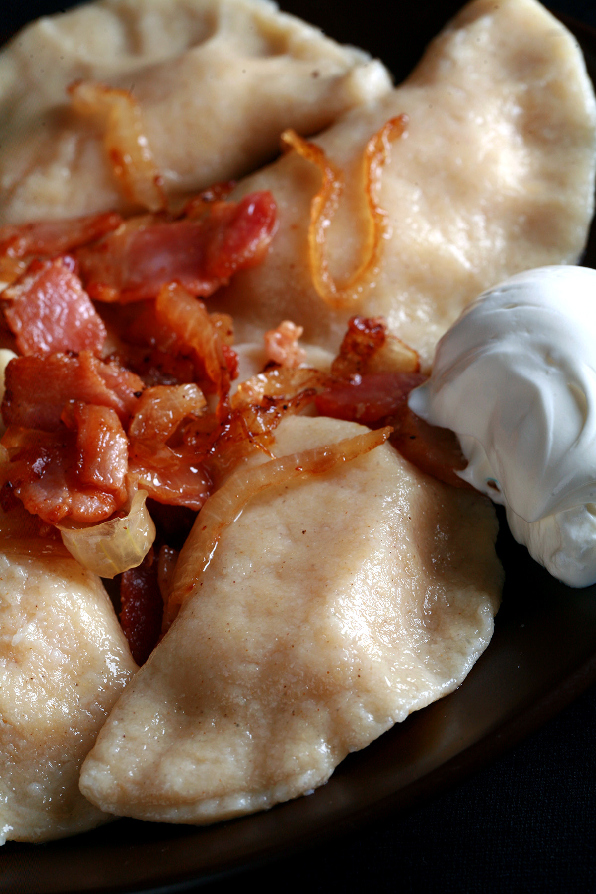 A plate of gluten-free perogies, topped with bacon, fried onions, and sour cream.