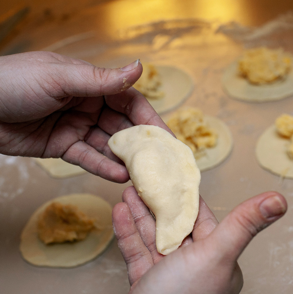 Two hands holding a newly formed perogie.