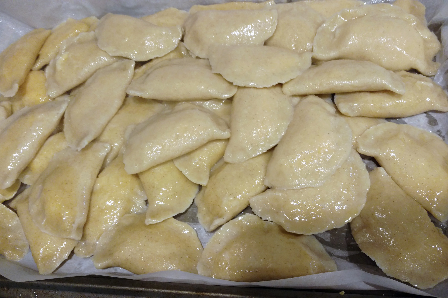 A pile of freshly boiled gluten-free perogies on a parchment lined baking sheet.