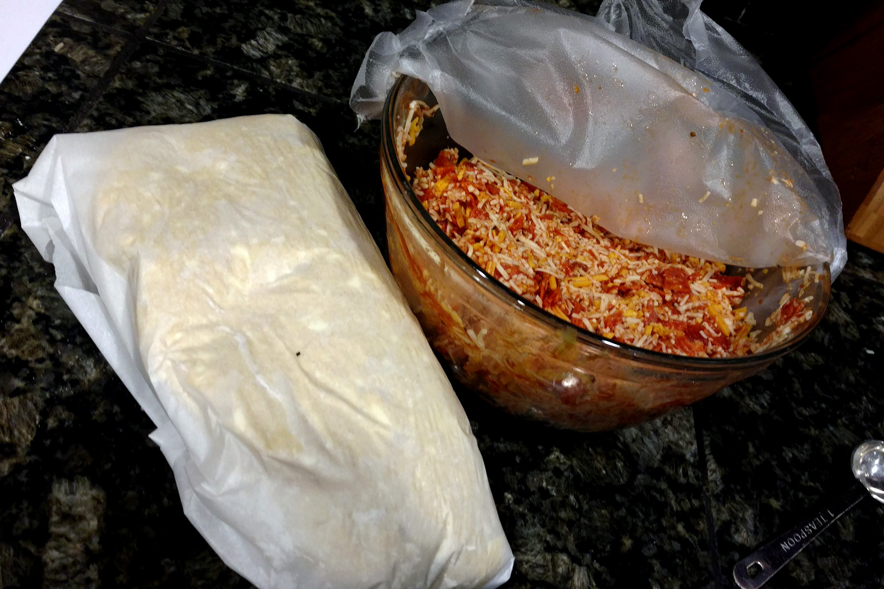 A wrapped lump of dough next to a bowl of the pizza filling.